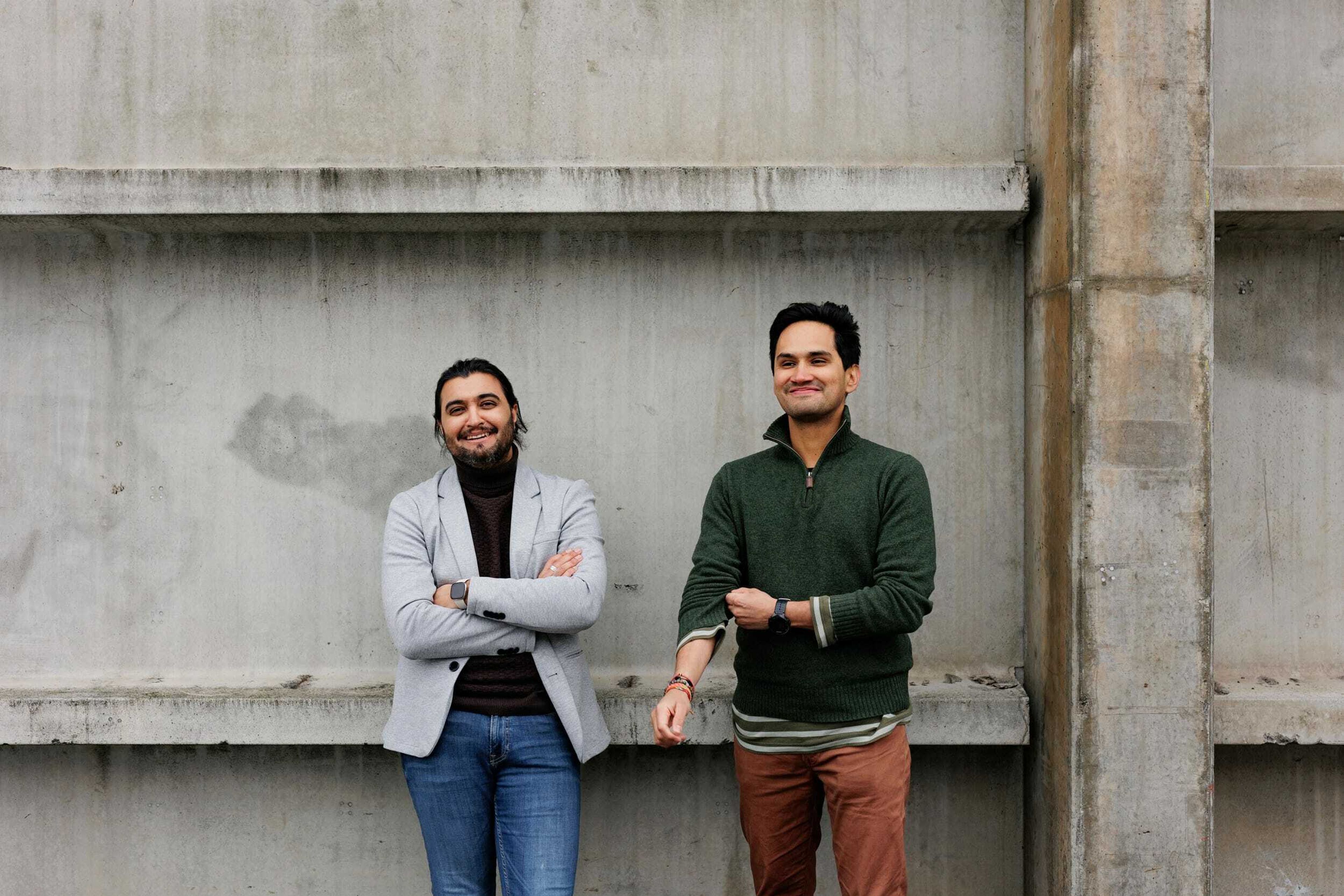 Foto av Mario Vahos og Osman Ilyas foran en betongvegg smilende.
