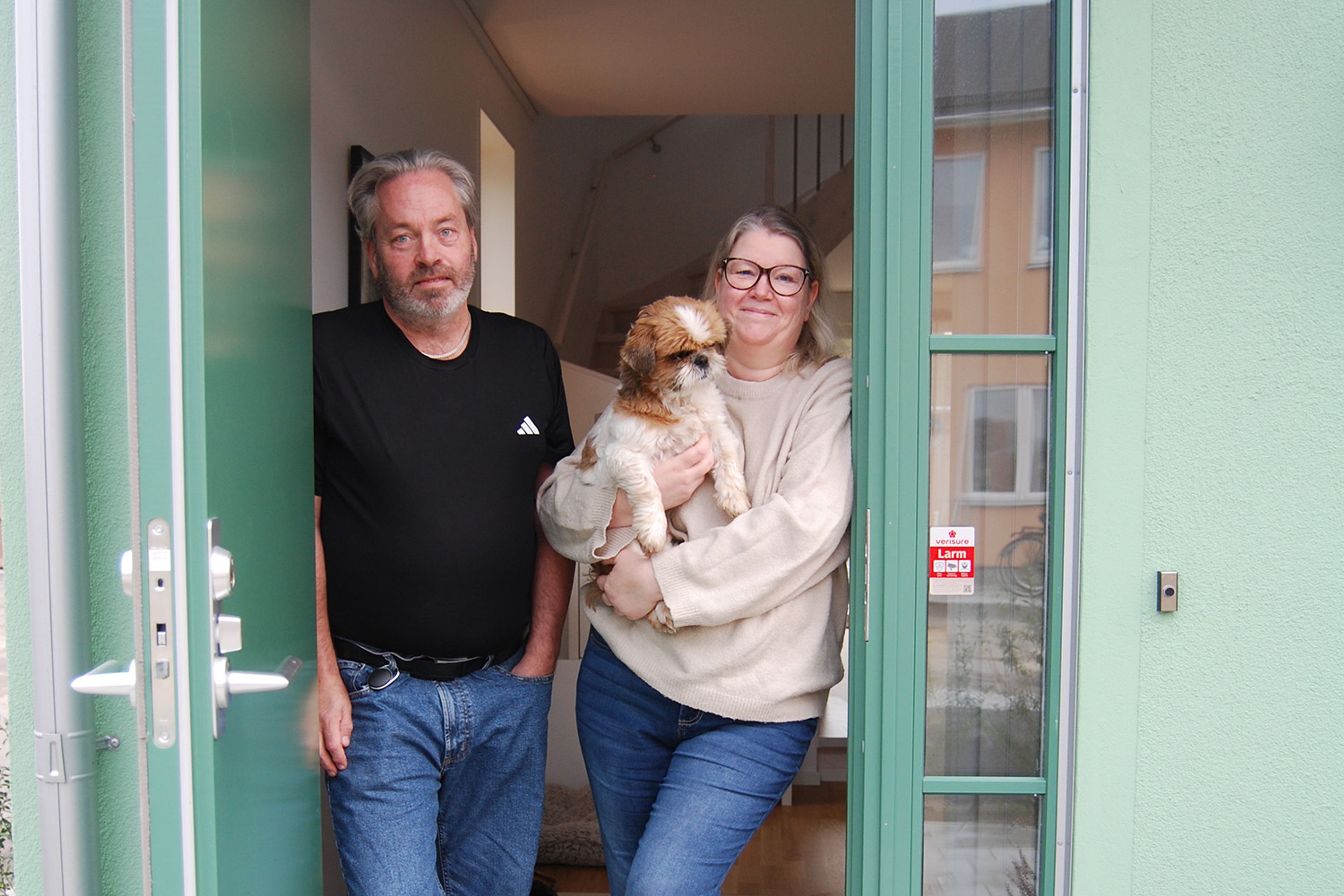 Foto på en man och en kvinna med en hund i famnen, ståendes i sin dörröppning