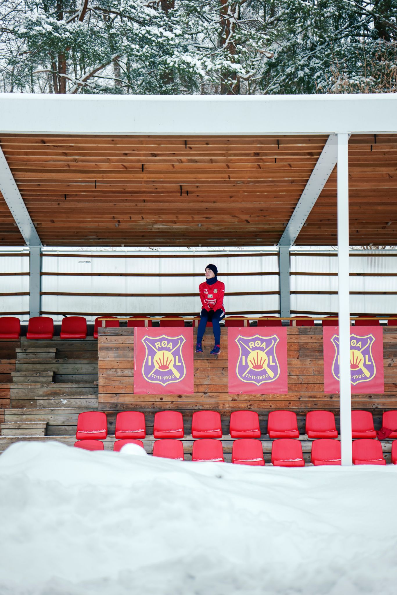 Sara sitter på tribunen og vi ser henne fra avstand.