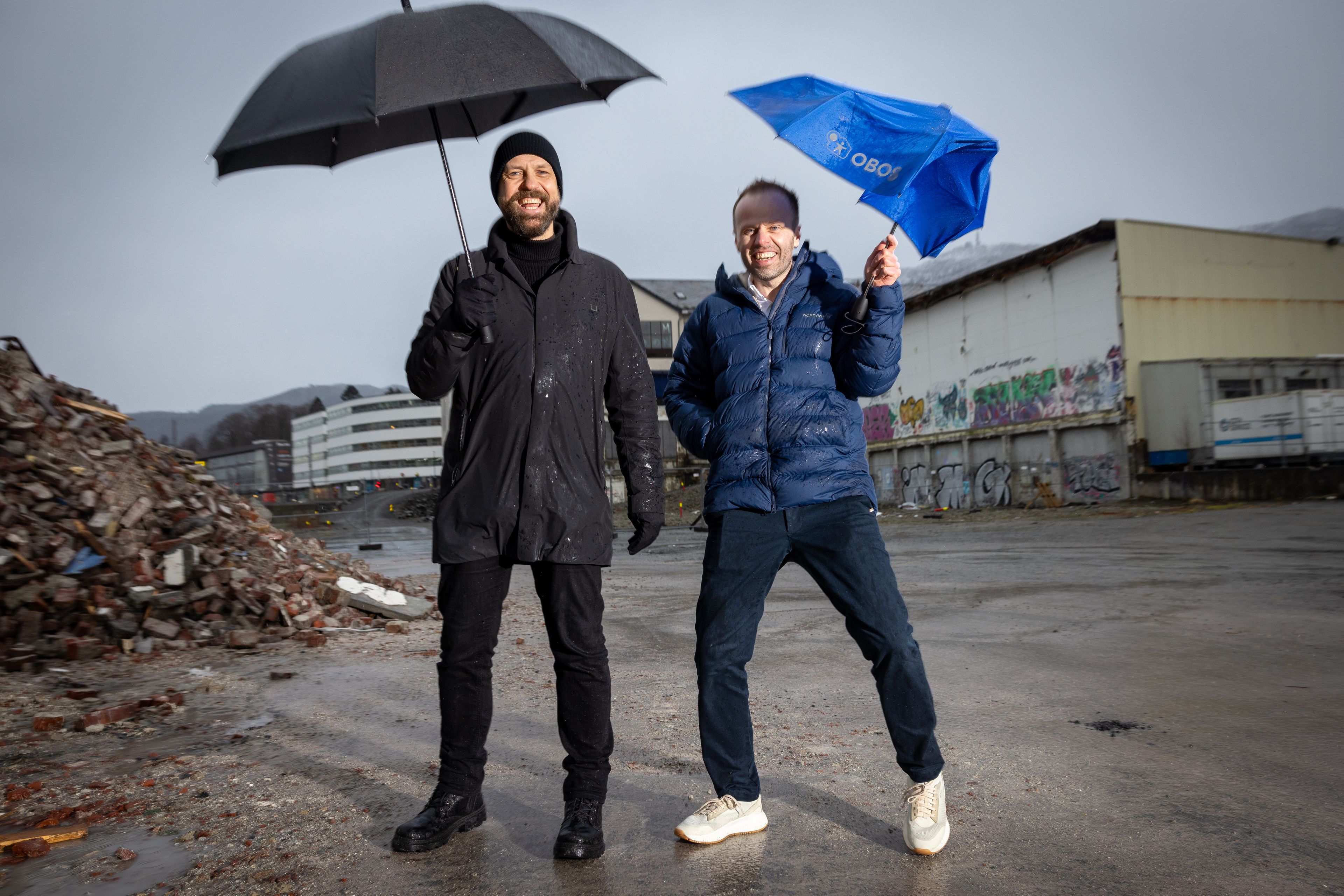 Arkitekt Fredrik Barth og prosjektleder Frode Rønhovde smiler i vind og regn på tomten der Bergensmeieriet skal bygges.