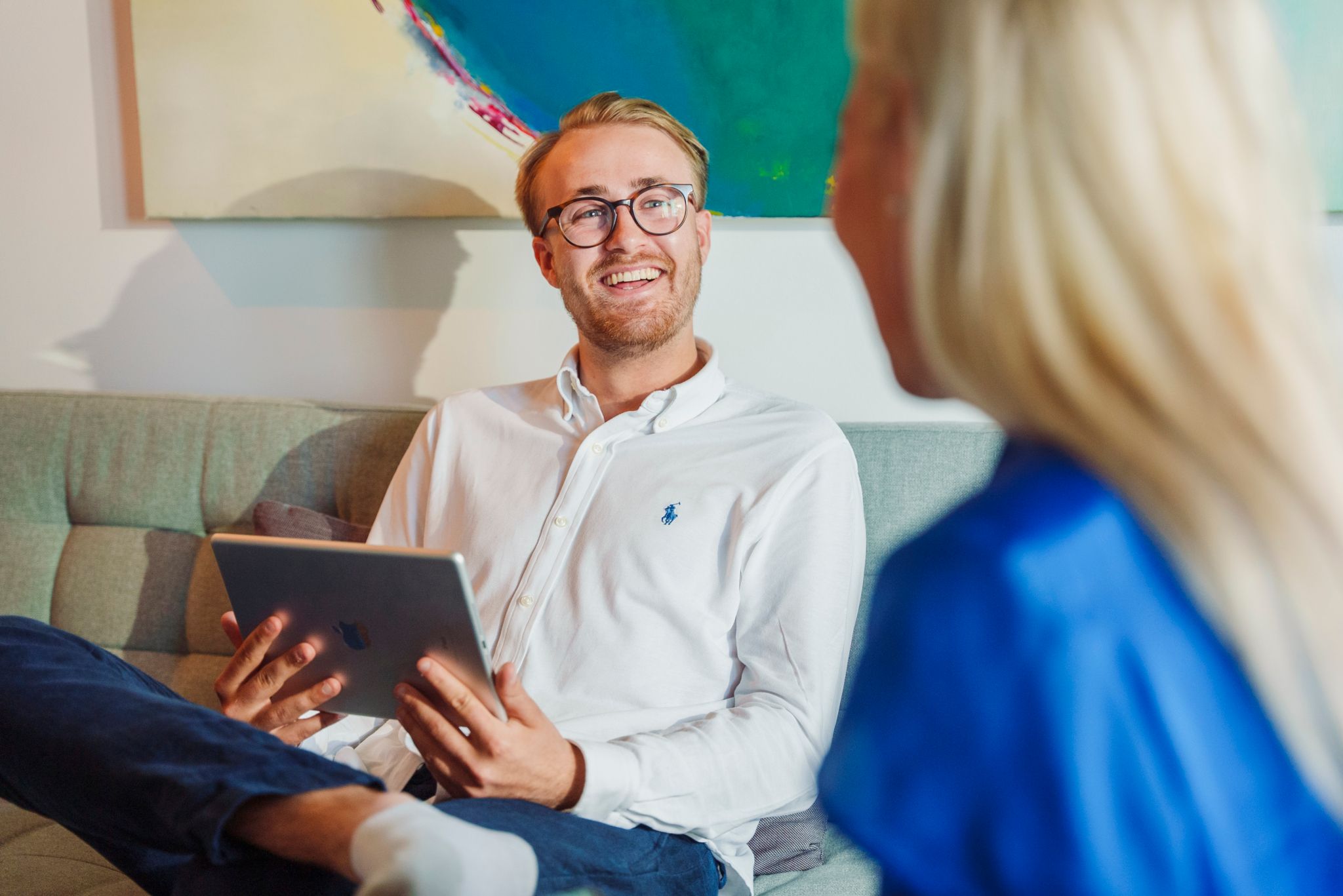 En mann sitter i en sofa med iPaden i henda. Han ser mot ei dame ved siden av seg og smiler.