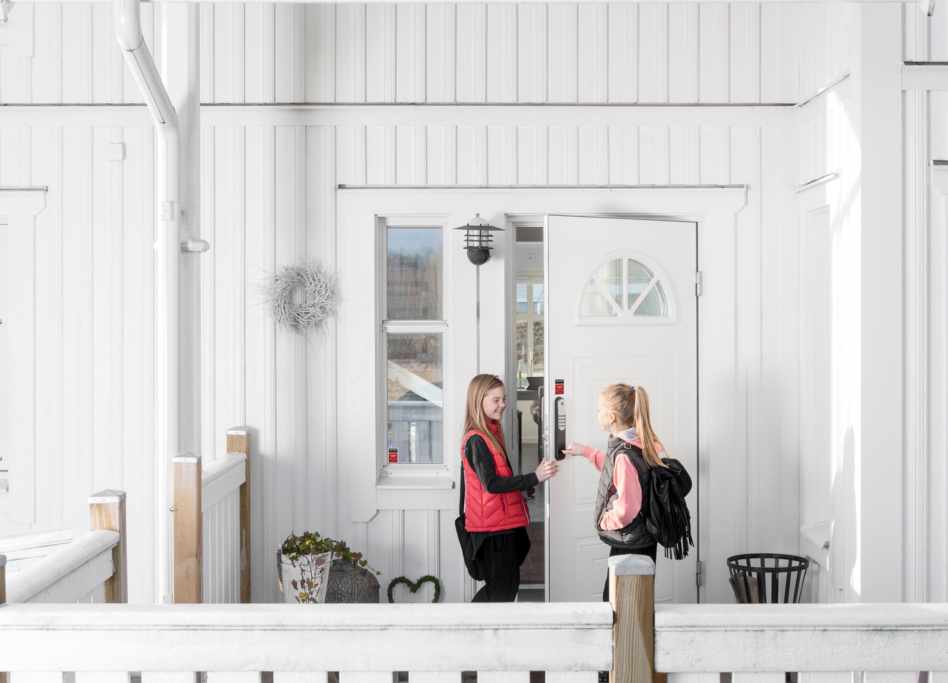 To jenter låser opp koden på døra som er koblet til alarmen. Det er et hvitt hus.