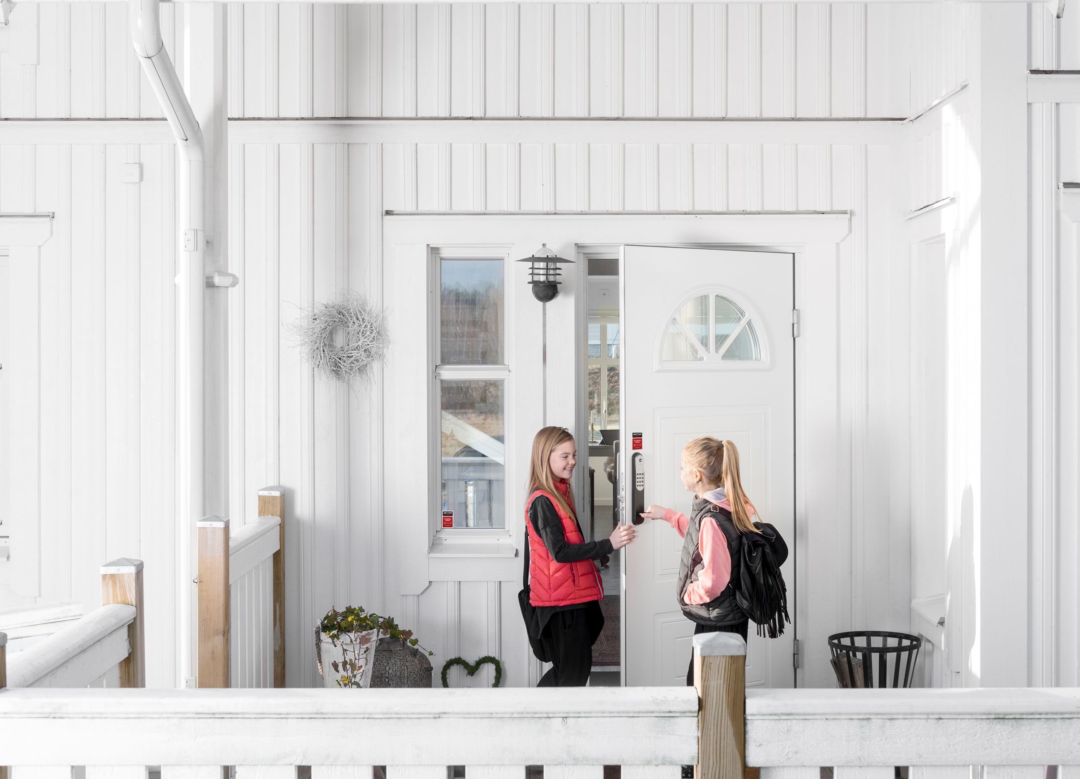 To jenter låser opp koden på døra som er koblet til alarmen. Det er et hvitt hus.