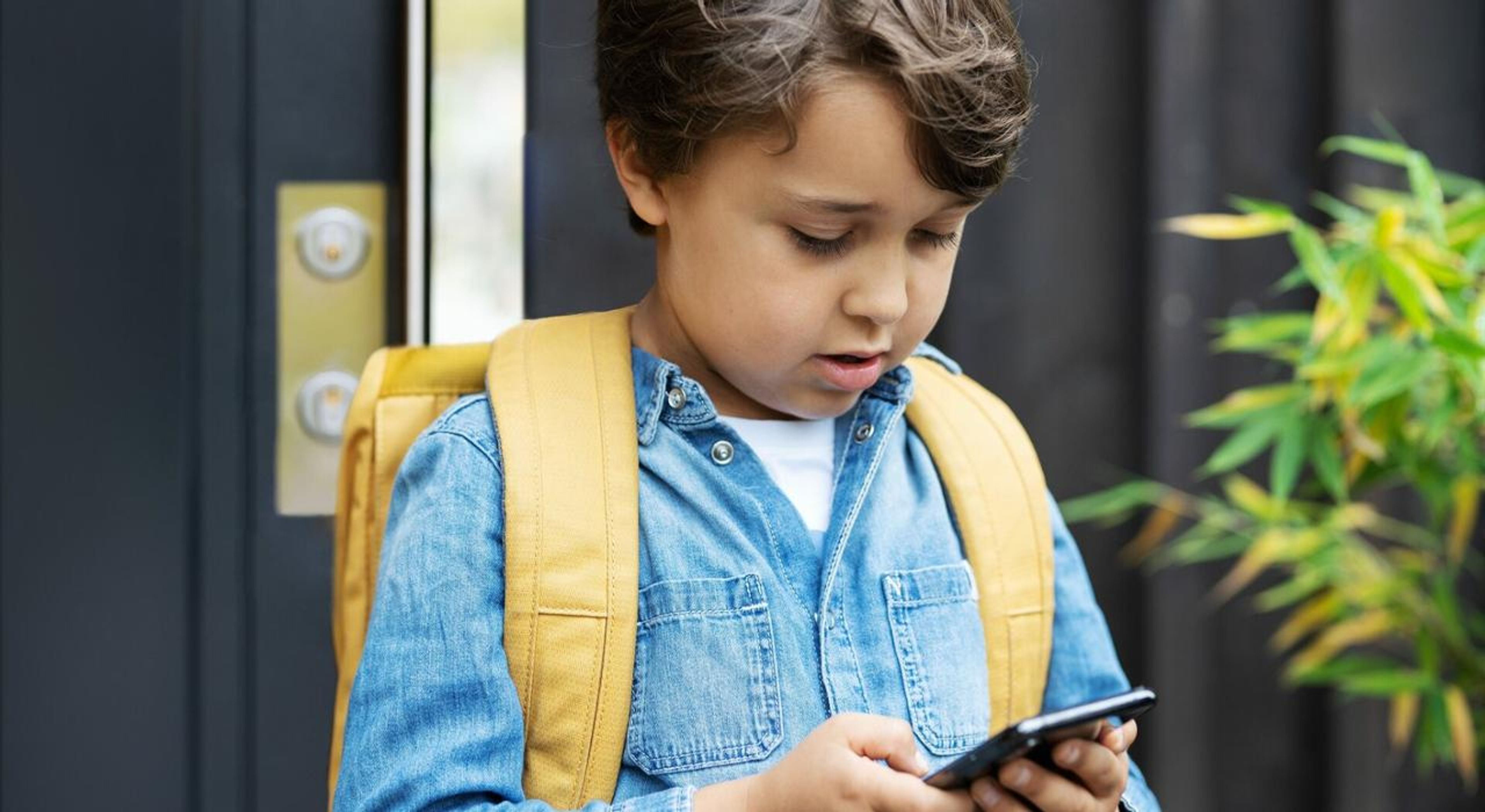 En ung gutt ser på mobilen sin i det han kommer ut av boligen sin.