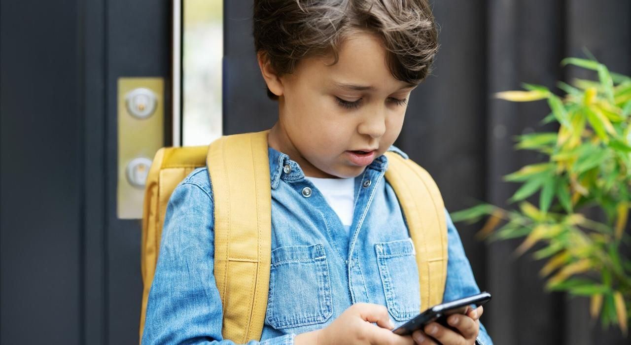 En ung gutt ser på mobilen sin i det han kommer ut av boligen sin.