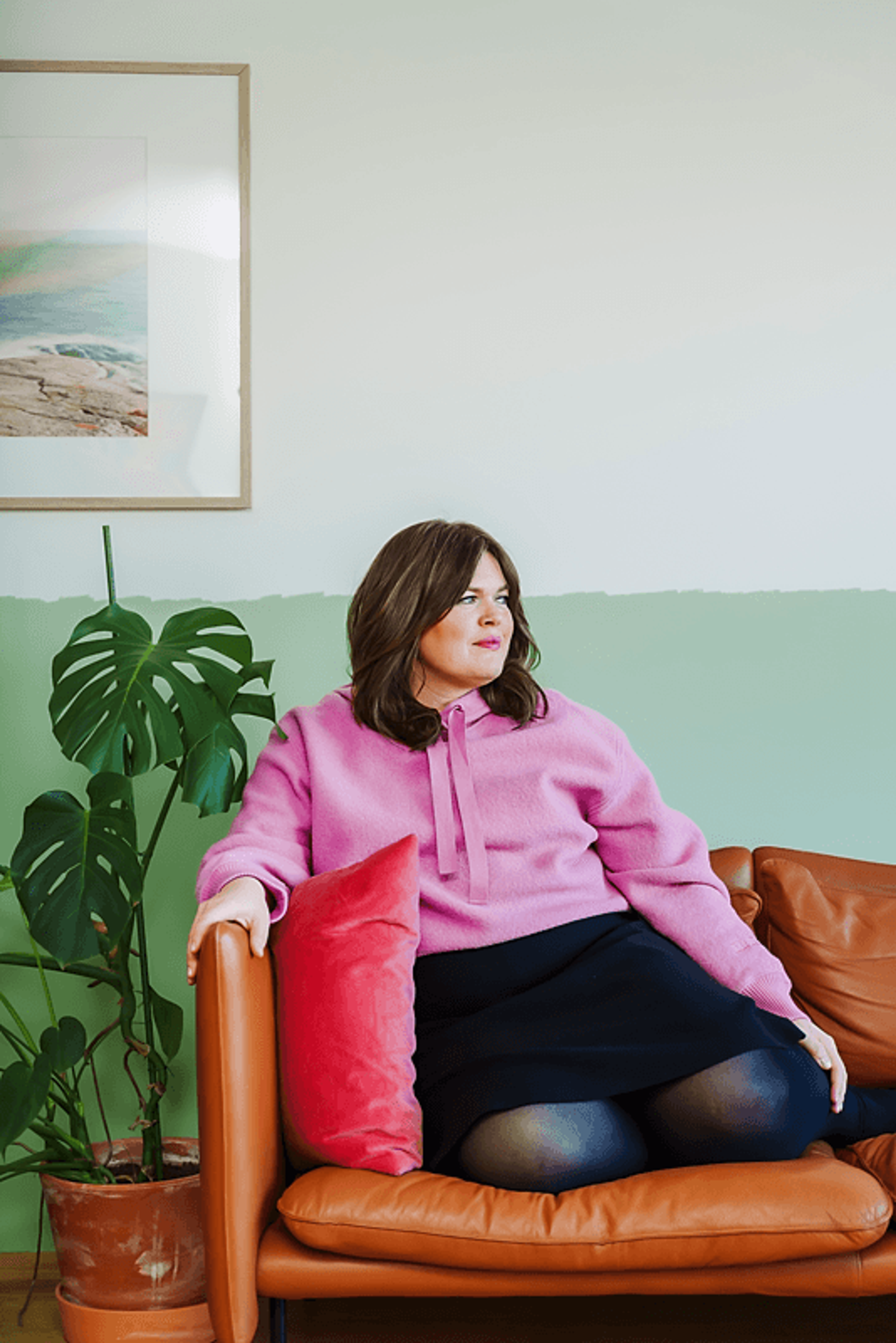 Ane sitter i sofaen sin i en rosa genser og et svart skjørt