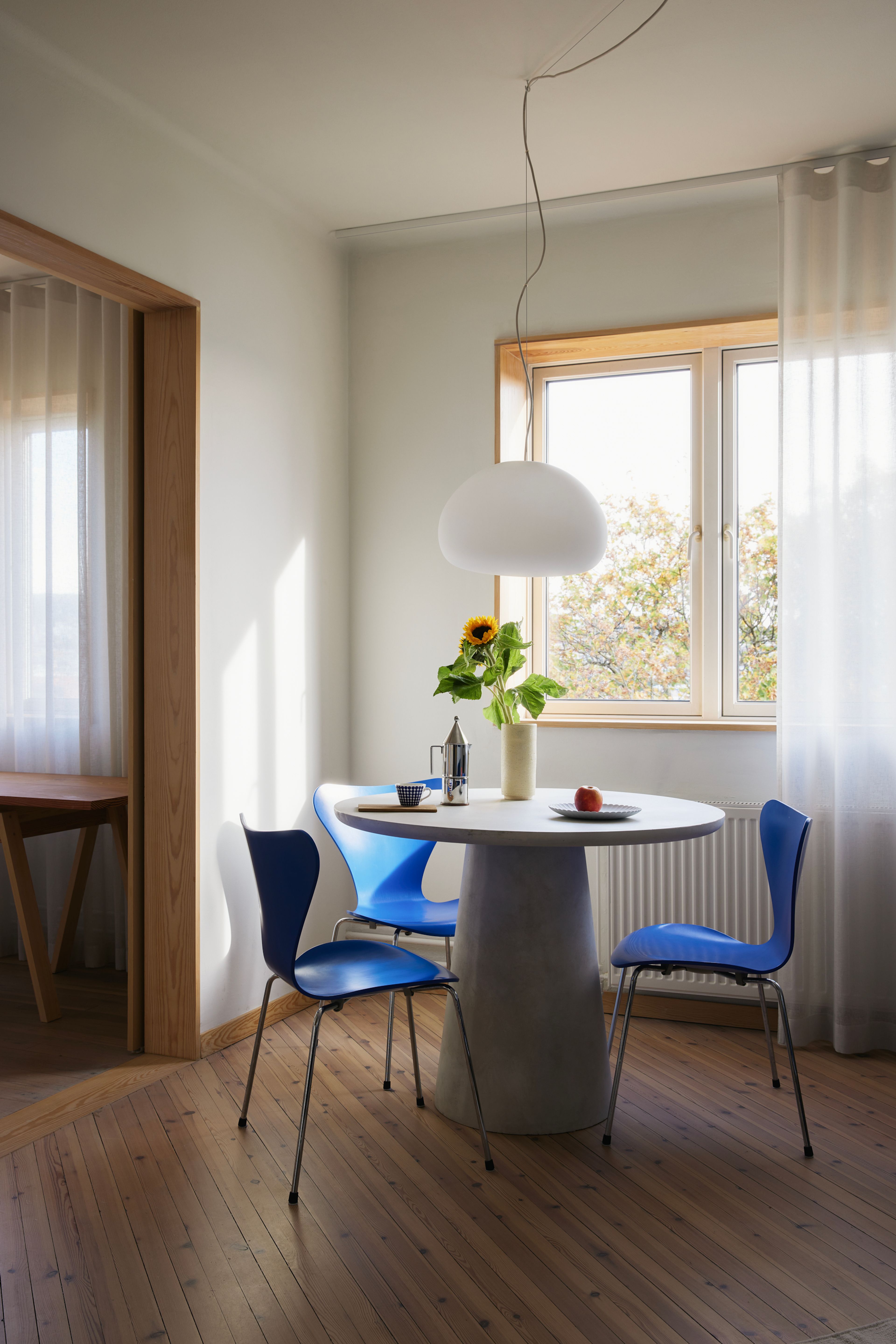 Et spisebord med blå stoler, en vase med solsikker og en taklampe som henger over bordet.