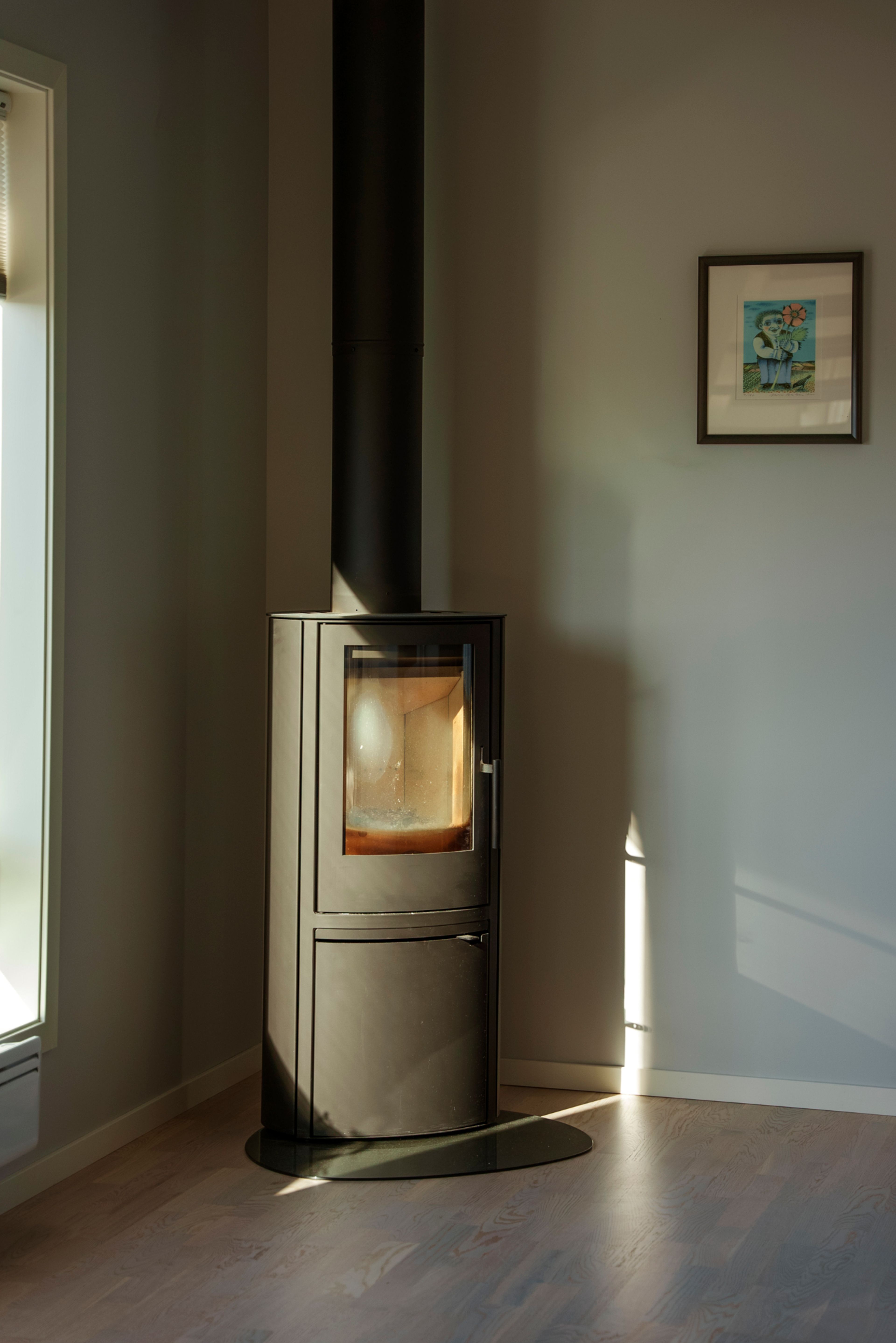 En svart peis mot en grå vegg hvor et lite bilde henger skrått over peisen.