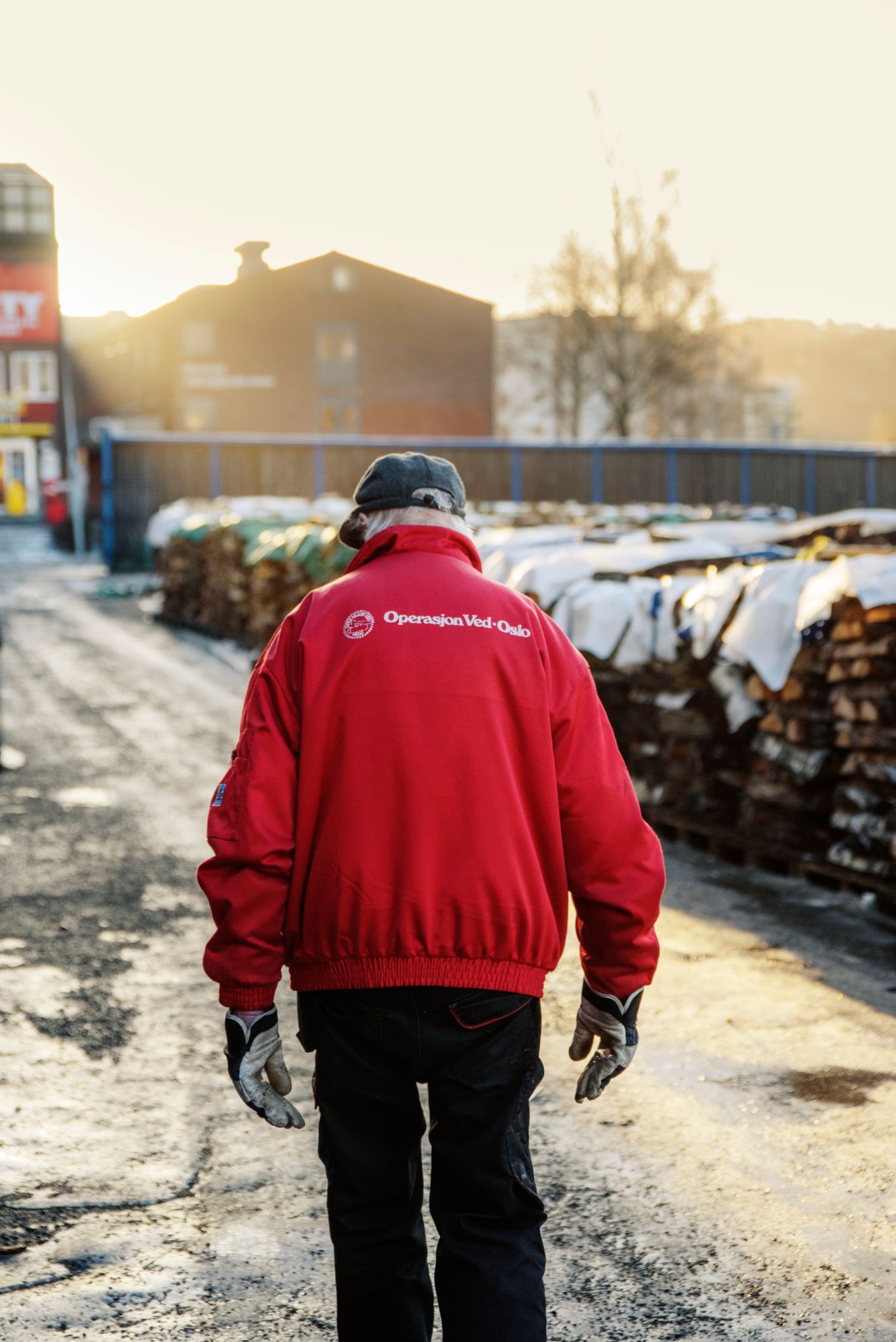 En av de frivillige i Operasjon Ved går langs rader med ved, med ryggen til bildet, i rød jakke.