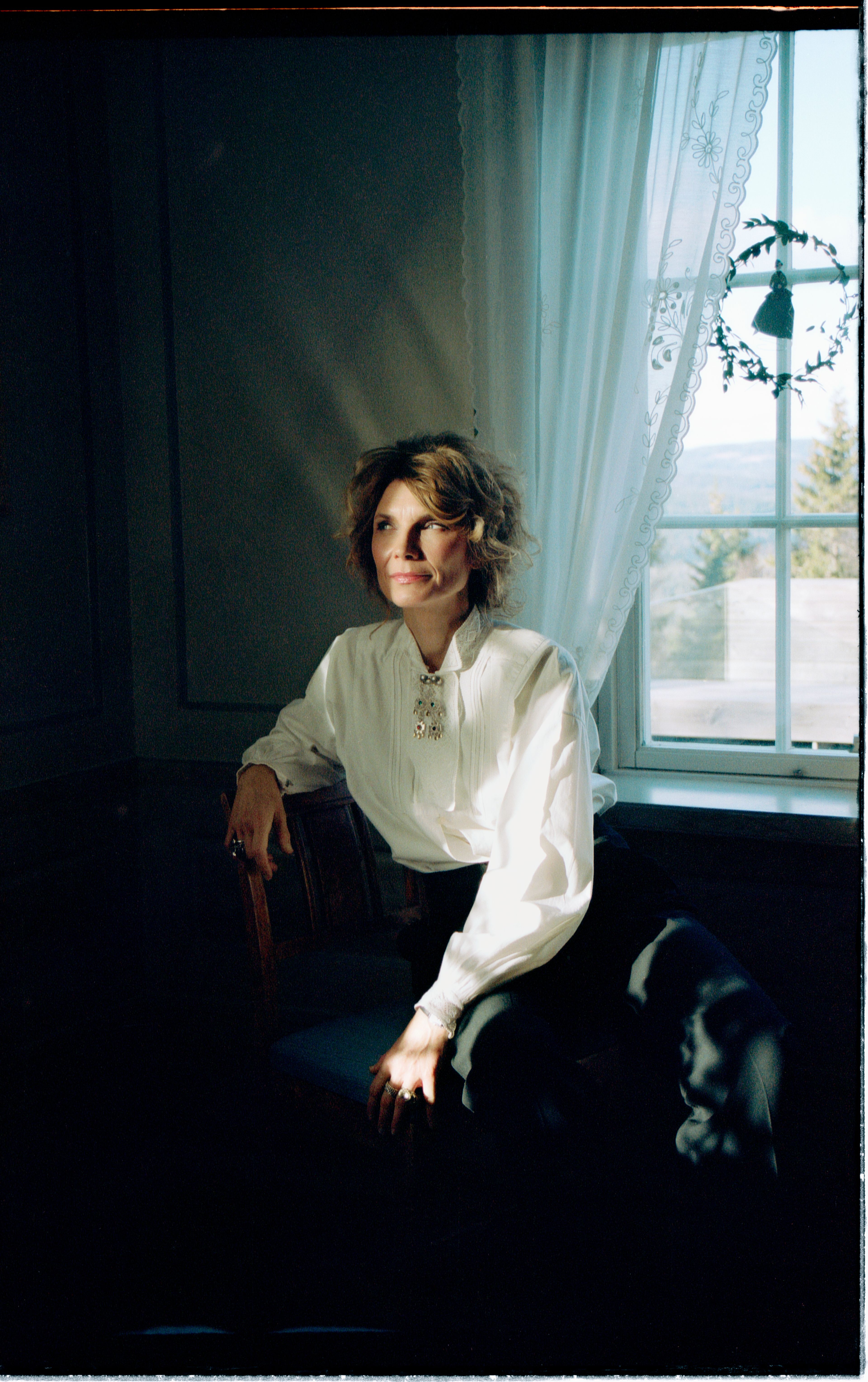 Et svart/hvitt bilde av Herborg Kråkvik som sitter i en stue iført bunadskjorte.