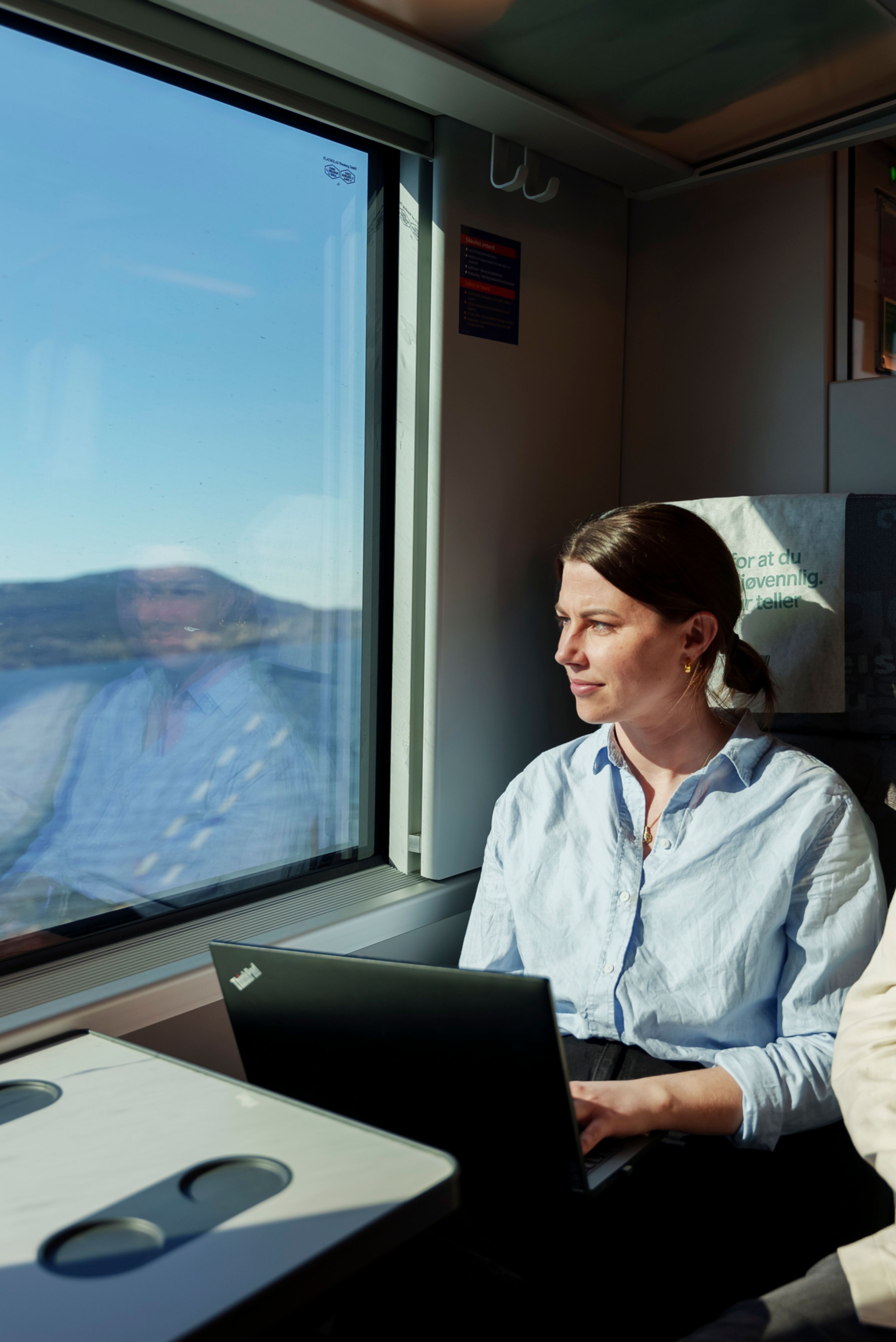 Stine sitter med PC i fanget og kikker ut over Mjøsa fra togvinduet.
