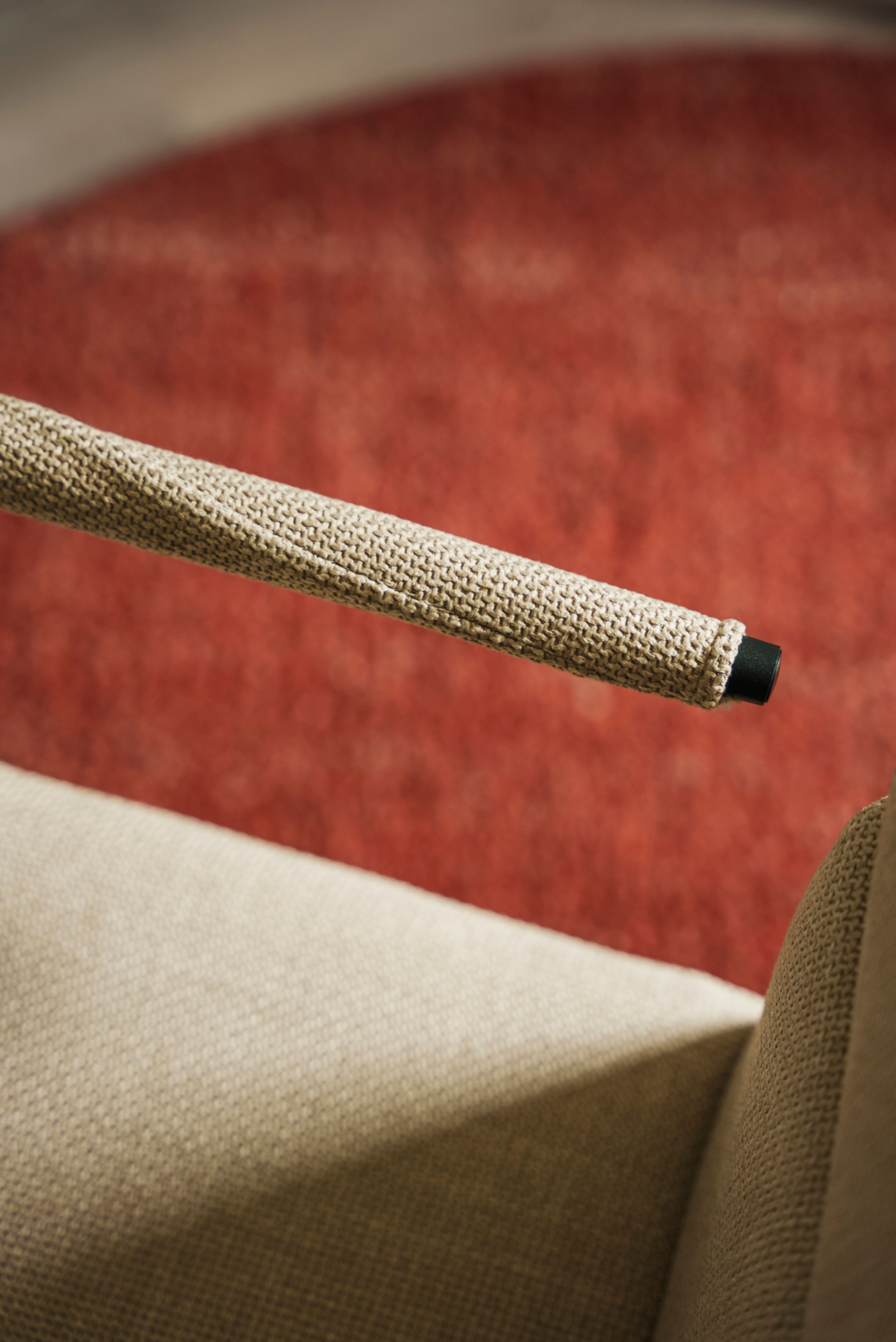 Armlenet til en kontor stol i beige, med rødt teppe i bakgrunnen.