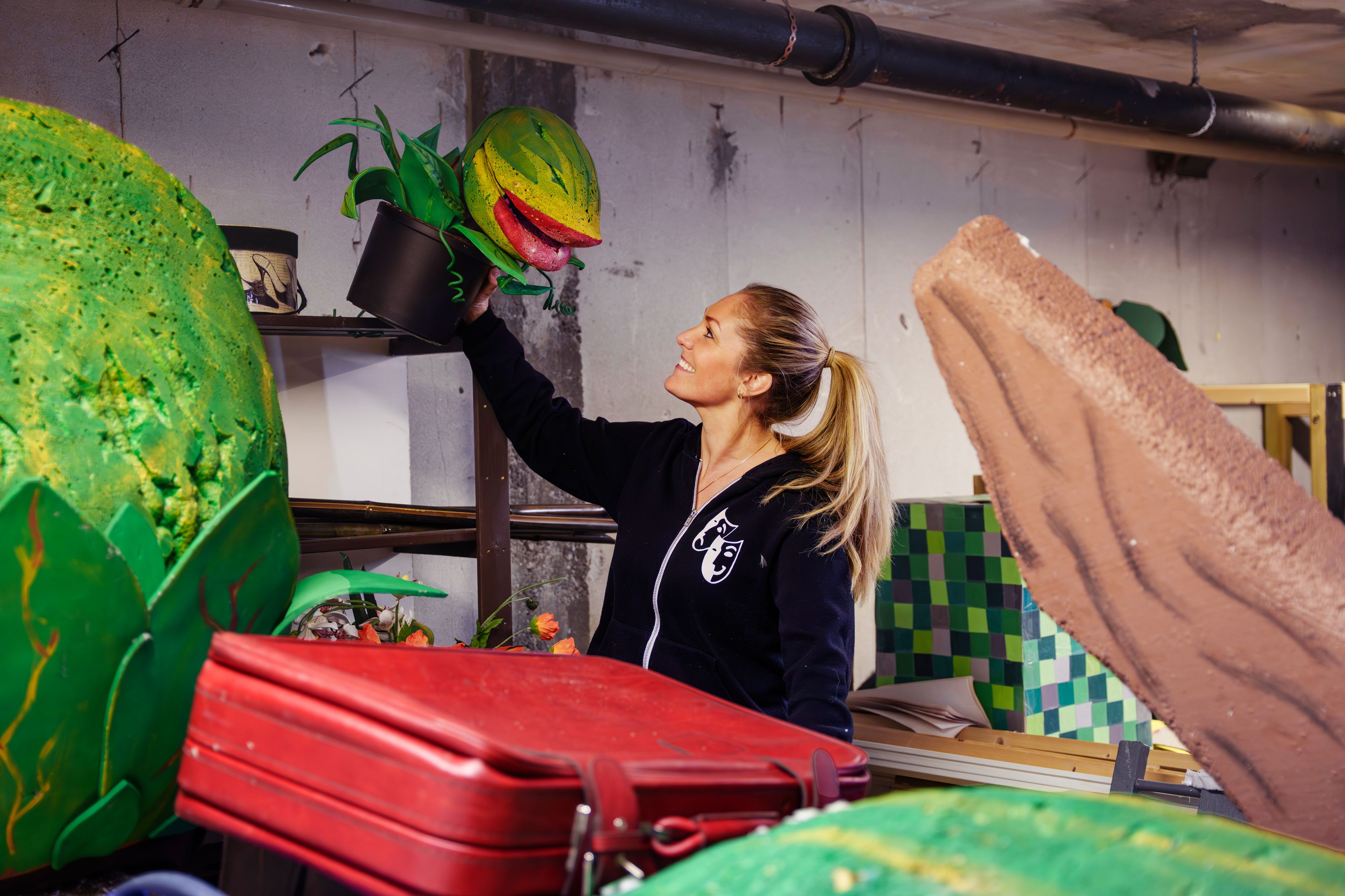 Mie Andberg løfter en stor håndlaget kjøttetende plante-rekvisitt opp i kulisseverkstedet til Action Teater.