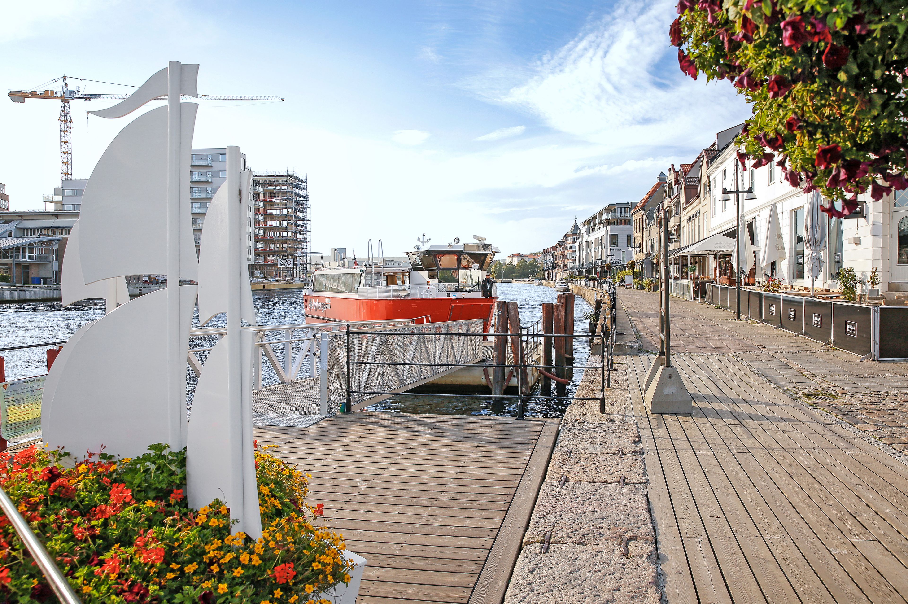 Bilde av byferga i Fredrikstad med havnepromenaden og blå himmel i bakgrunnen.