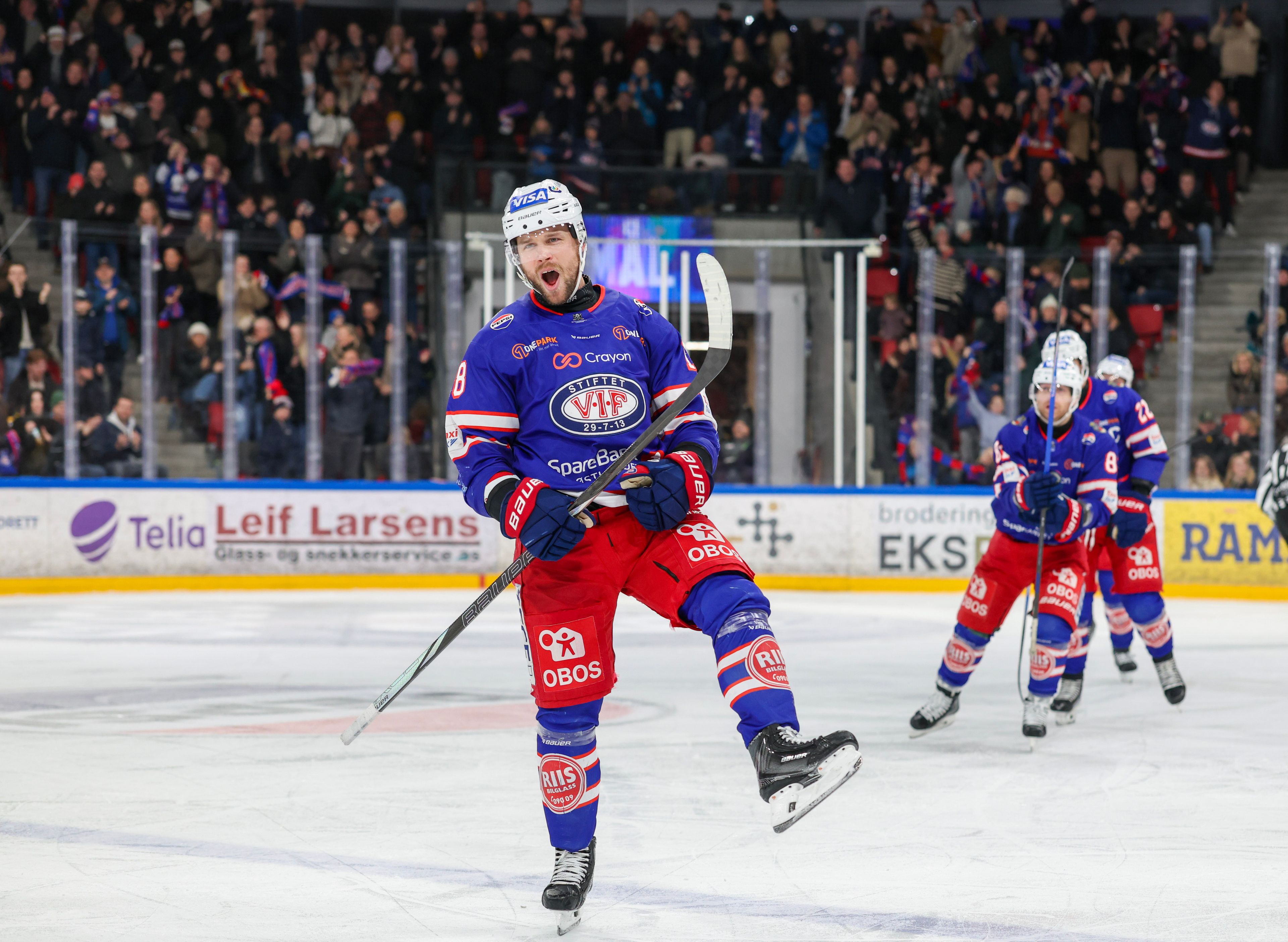En spiller på Vålerenga ishockey skøyter på én fot mot kamera mens han jubler. Bak ham kommer tre medspillere. 