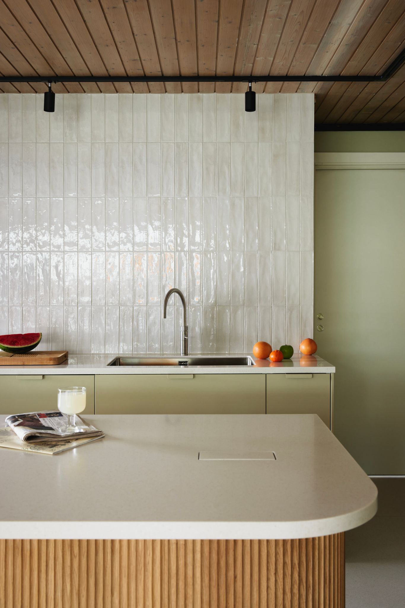 Et flislagt kjøkken med en kjøkkenøy. Veggene er malt i en olivengrønn farge.