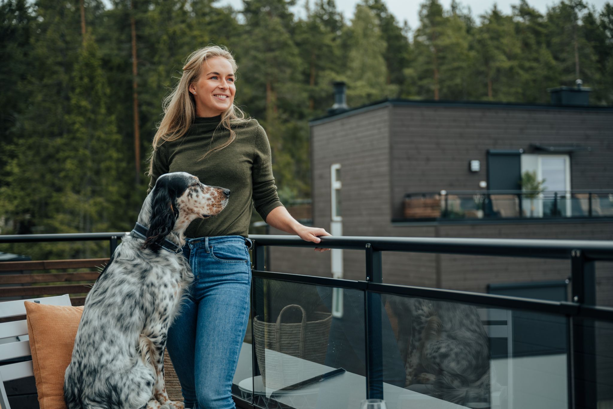 En kvinne og en hund ute på en terrasse i et OBOS Block Watne-hus, med utsikt mot et annet trehus.