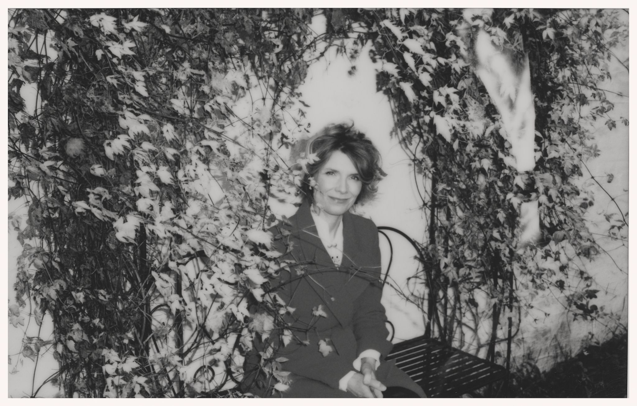 Herborg Kråkvik sitter på en benk under en busk.