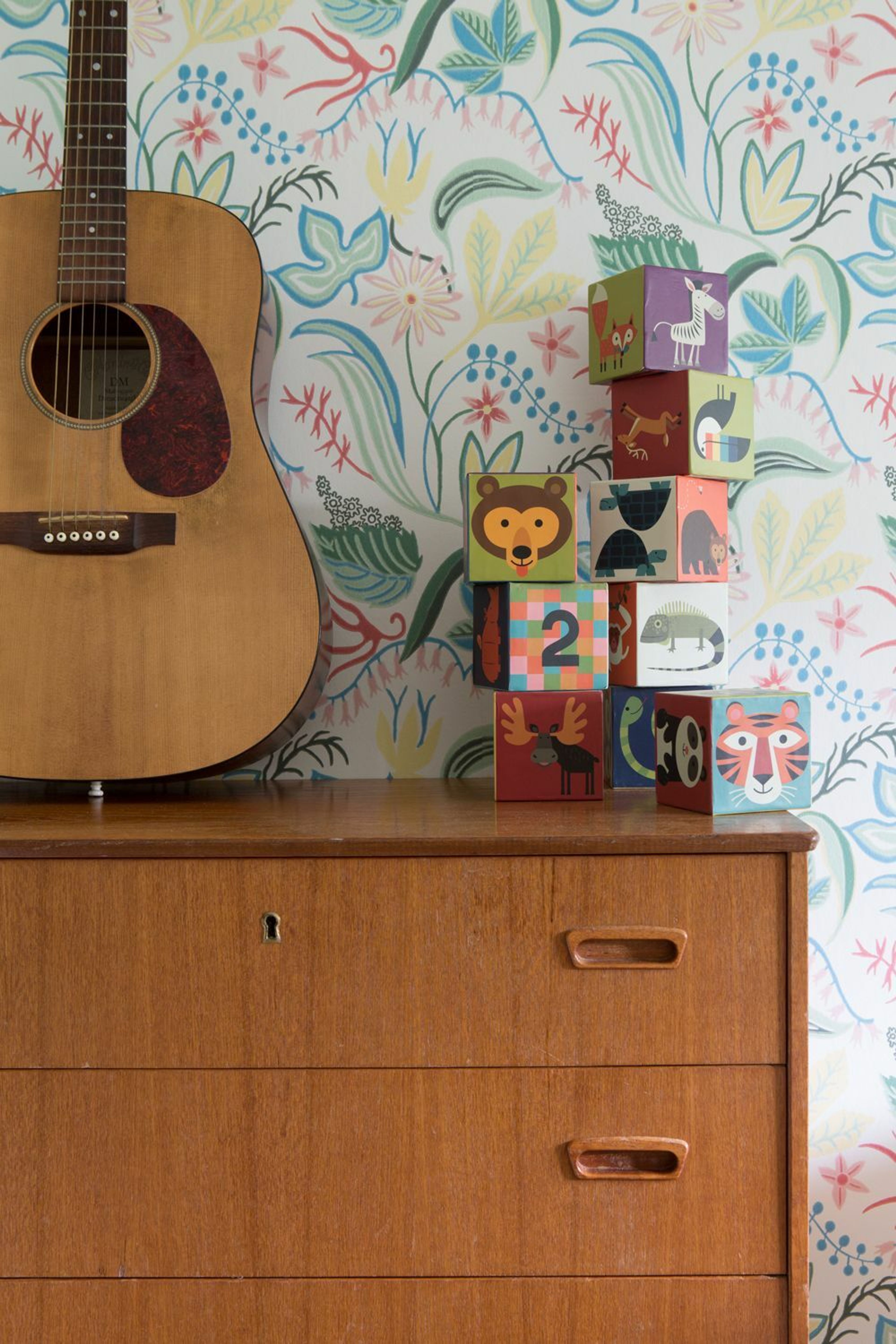 Brun retro kommode med en gitar stående oppå foran en tapetsert vegg.