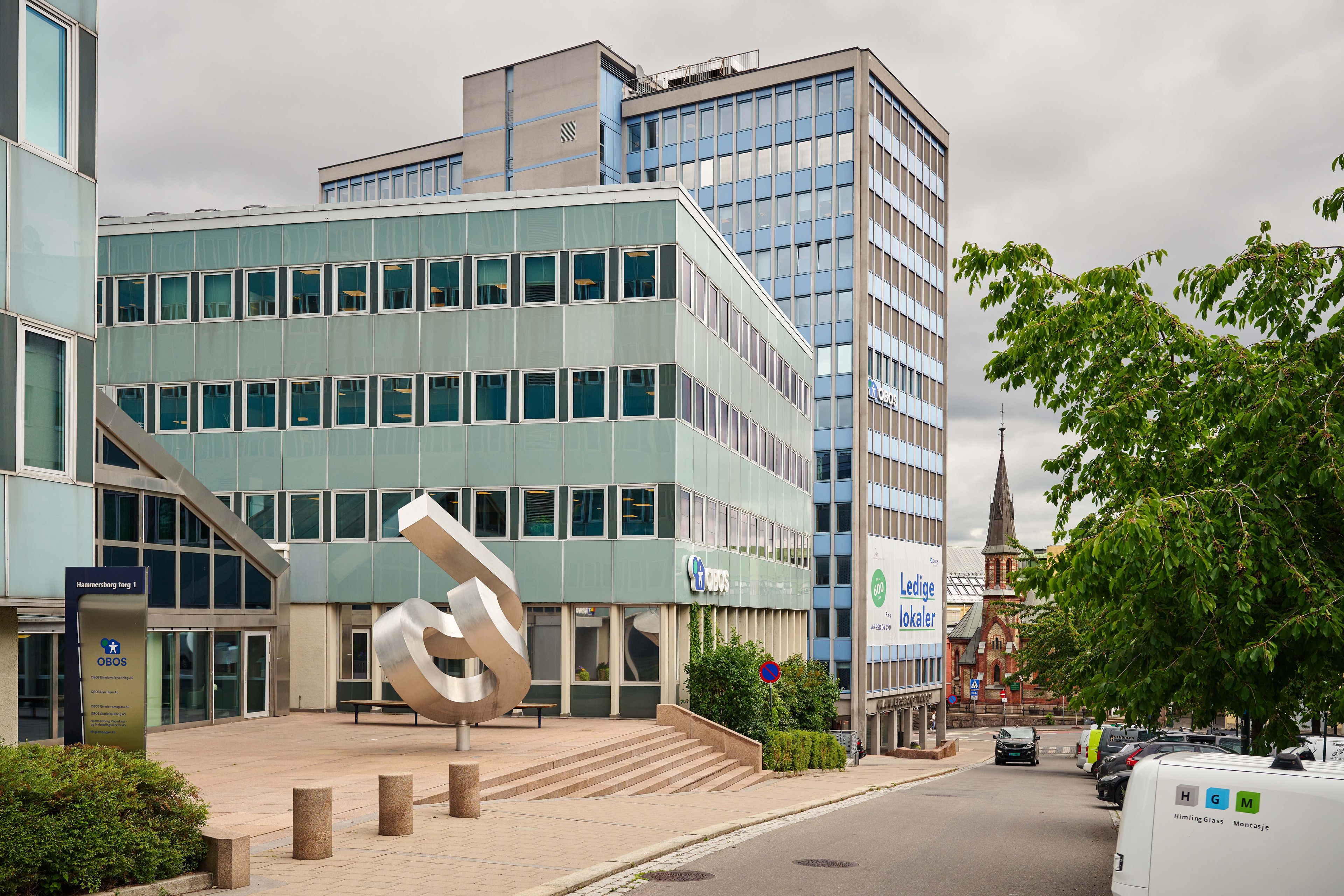 Foto av statuen ved inngangen, med høyblokk 3 og mellomblokka i bakgrunn.