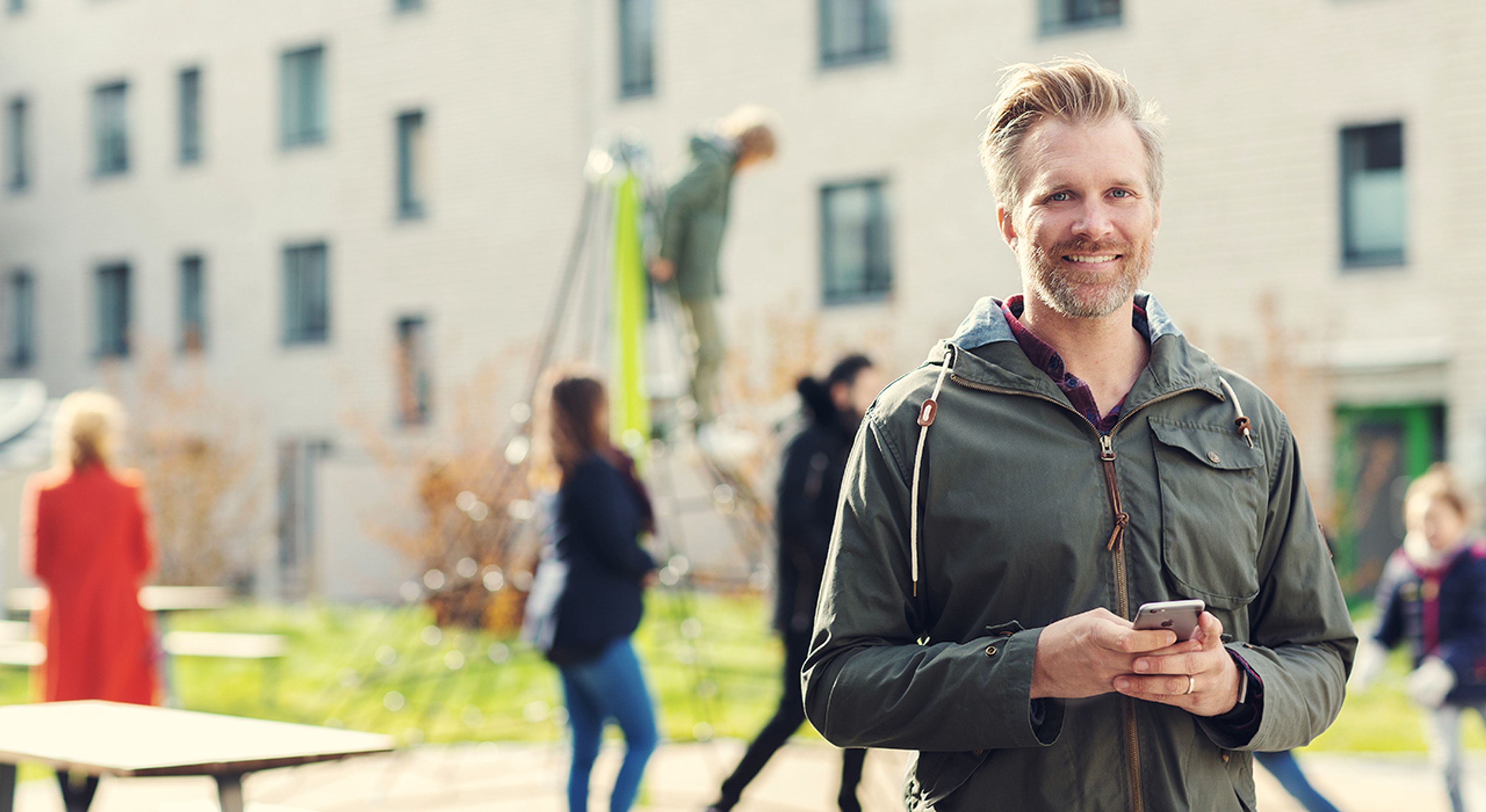 Ung voksen mann, trolig styreleder, i gårdsrom med flere beboere og barn i klatrestativ  i bakgrunnen.