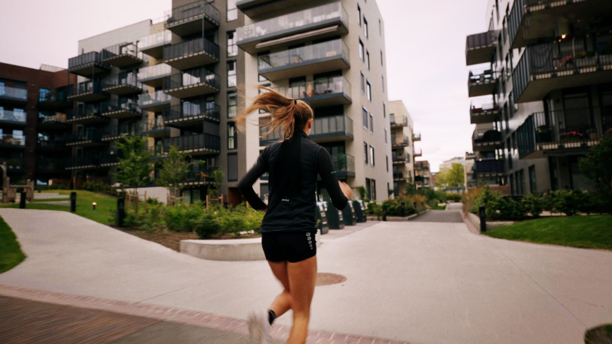 Sigrid løper med ryggen til mellom boligbygg i Frysjaparken.