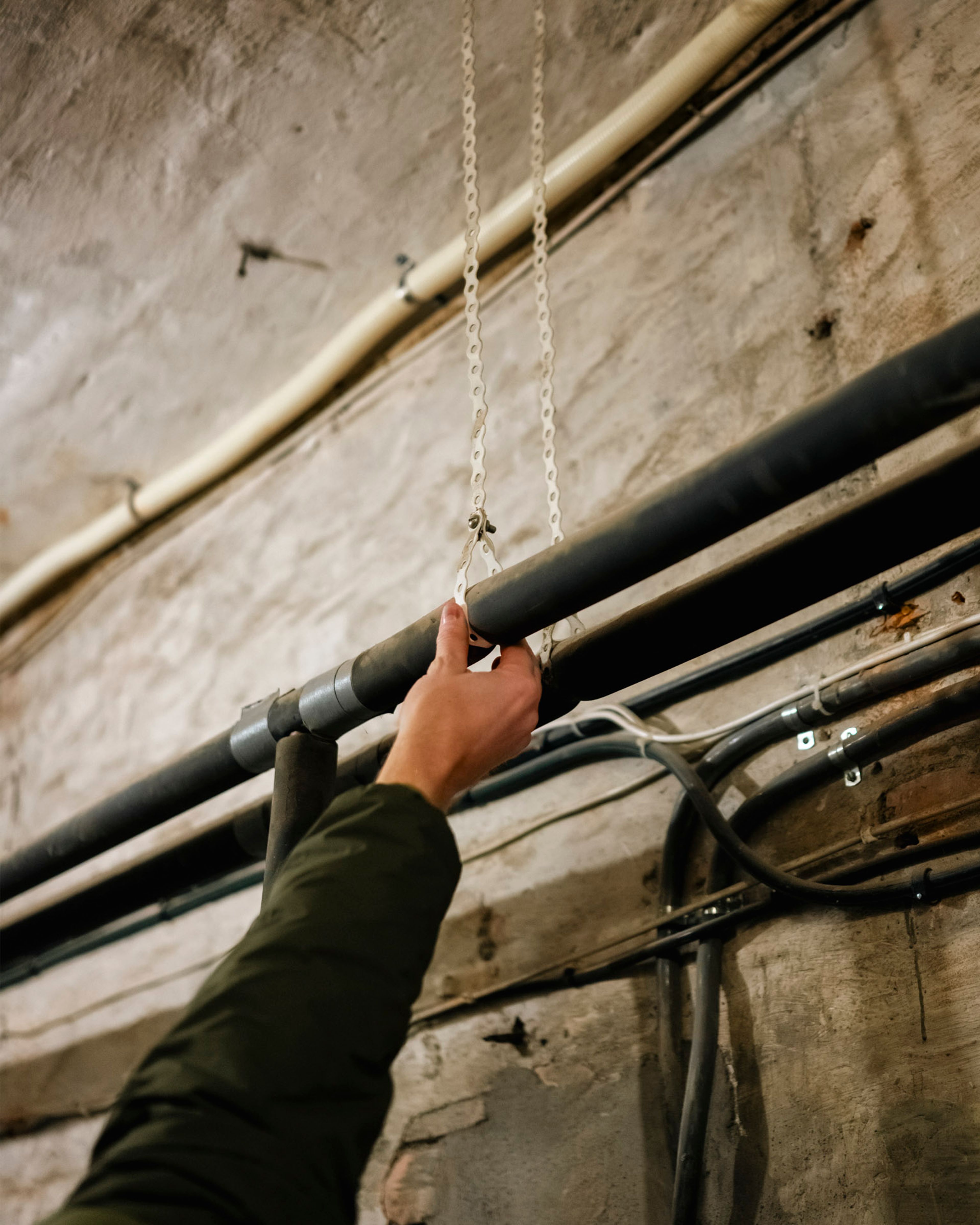 En hånd peker på tekniske rør i kjelleren i Markveien 2, der infrastrukturen gjør energitiltak utfordrende.