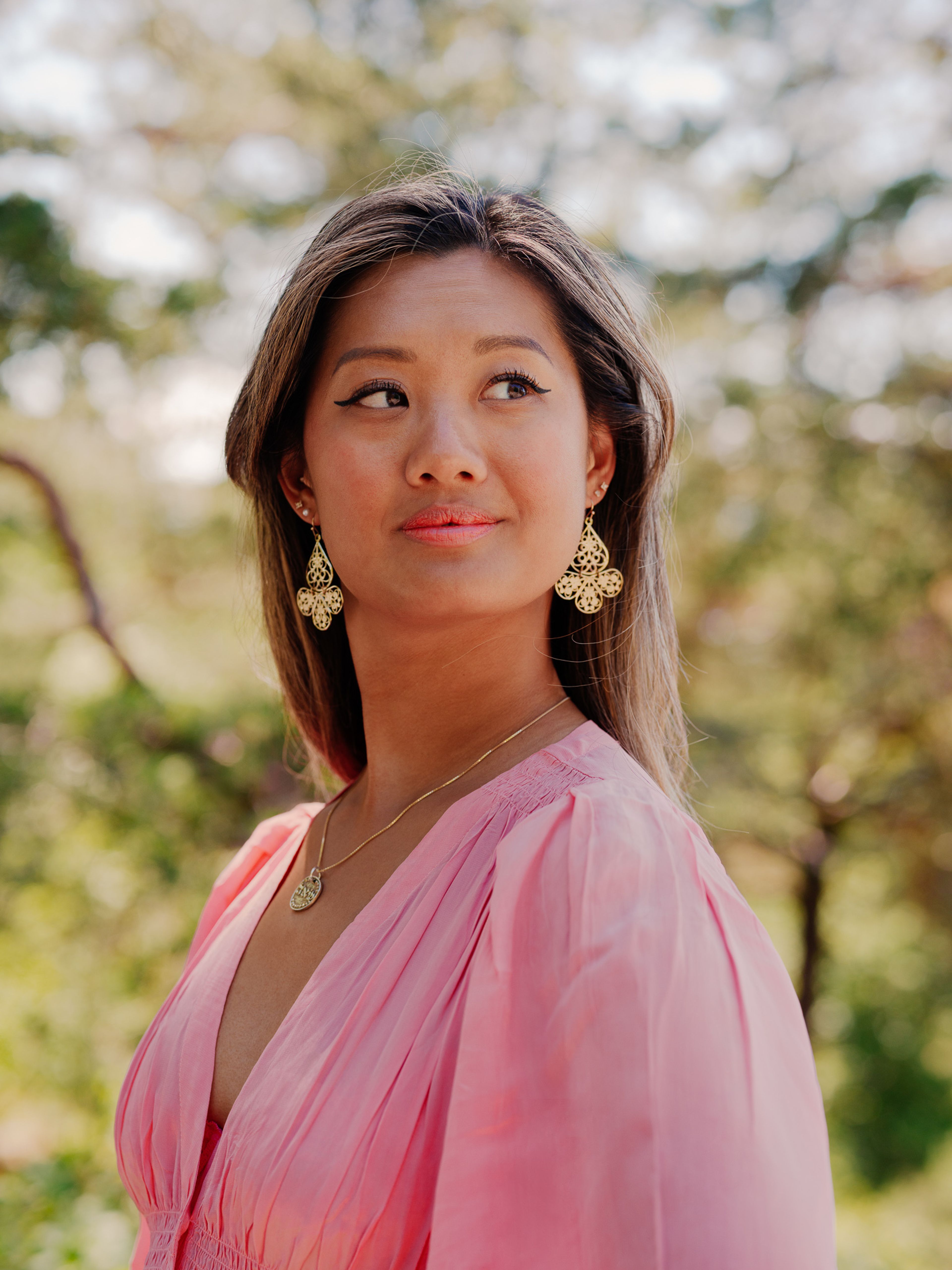 Catharina Chen står ute i skogen. Hun har på seg en rosa kjole, et smykke og matchende øredobber.