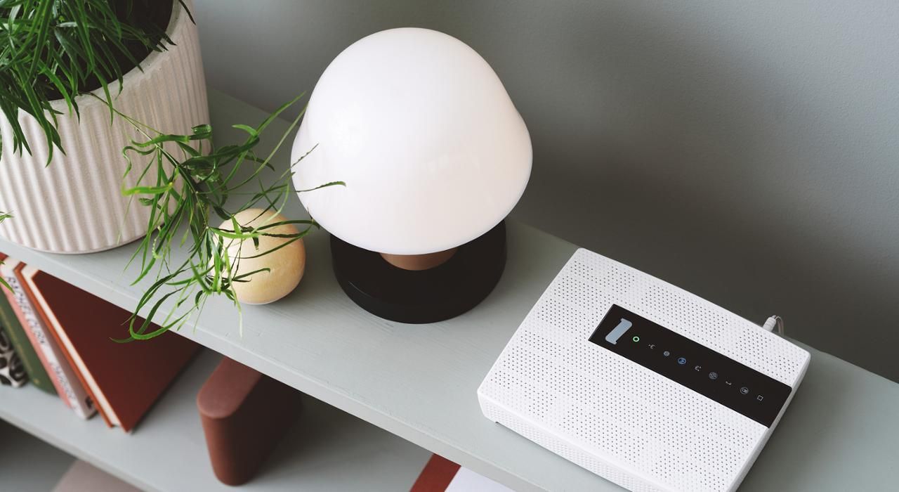 Foto av et konsollbord med et modem, lampe, noen bøker og noen planter.