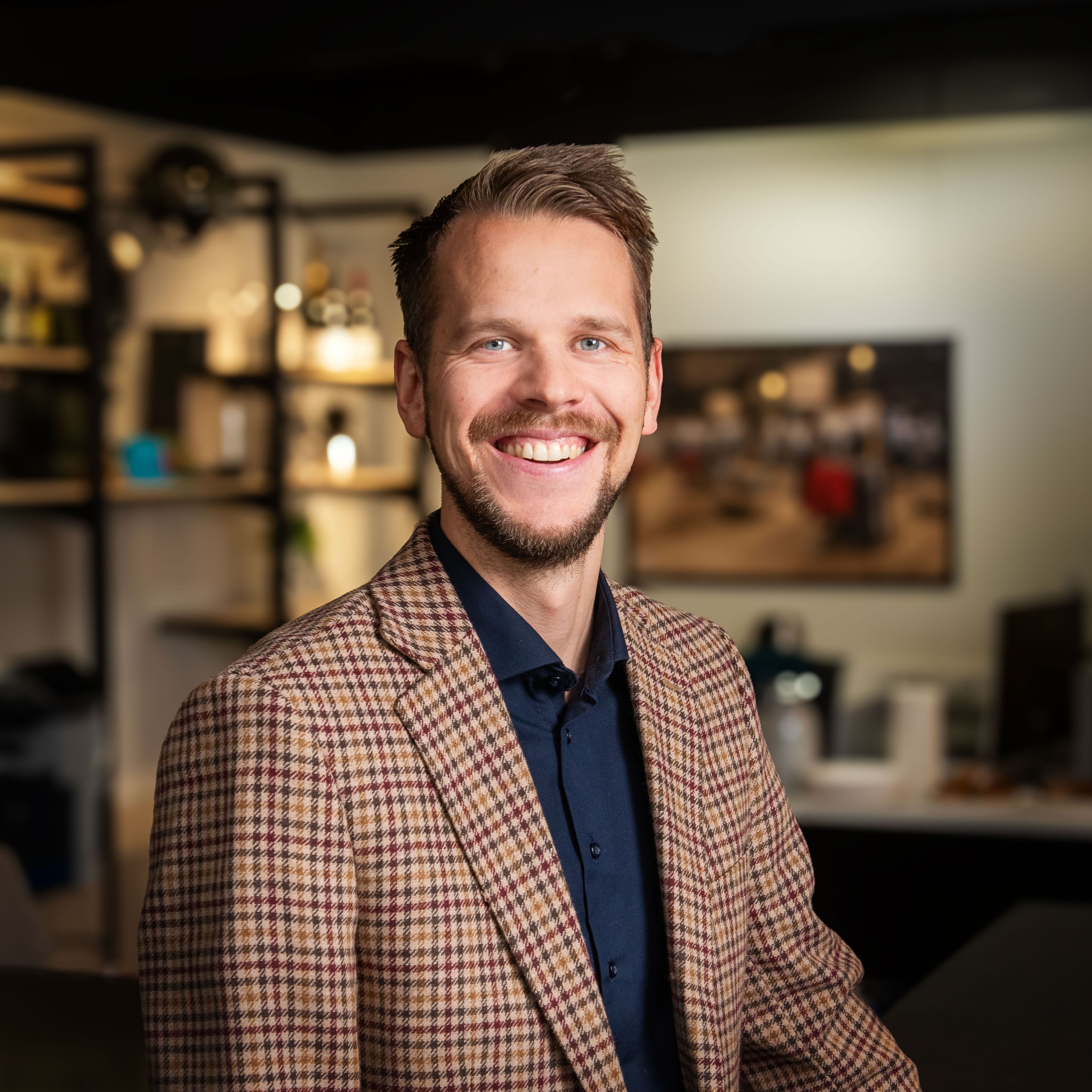 En mann i stripete skjorte ser mot kameraet og smiler. 
