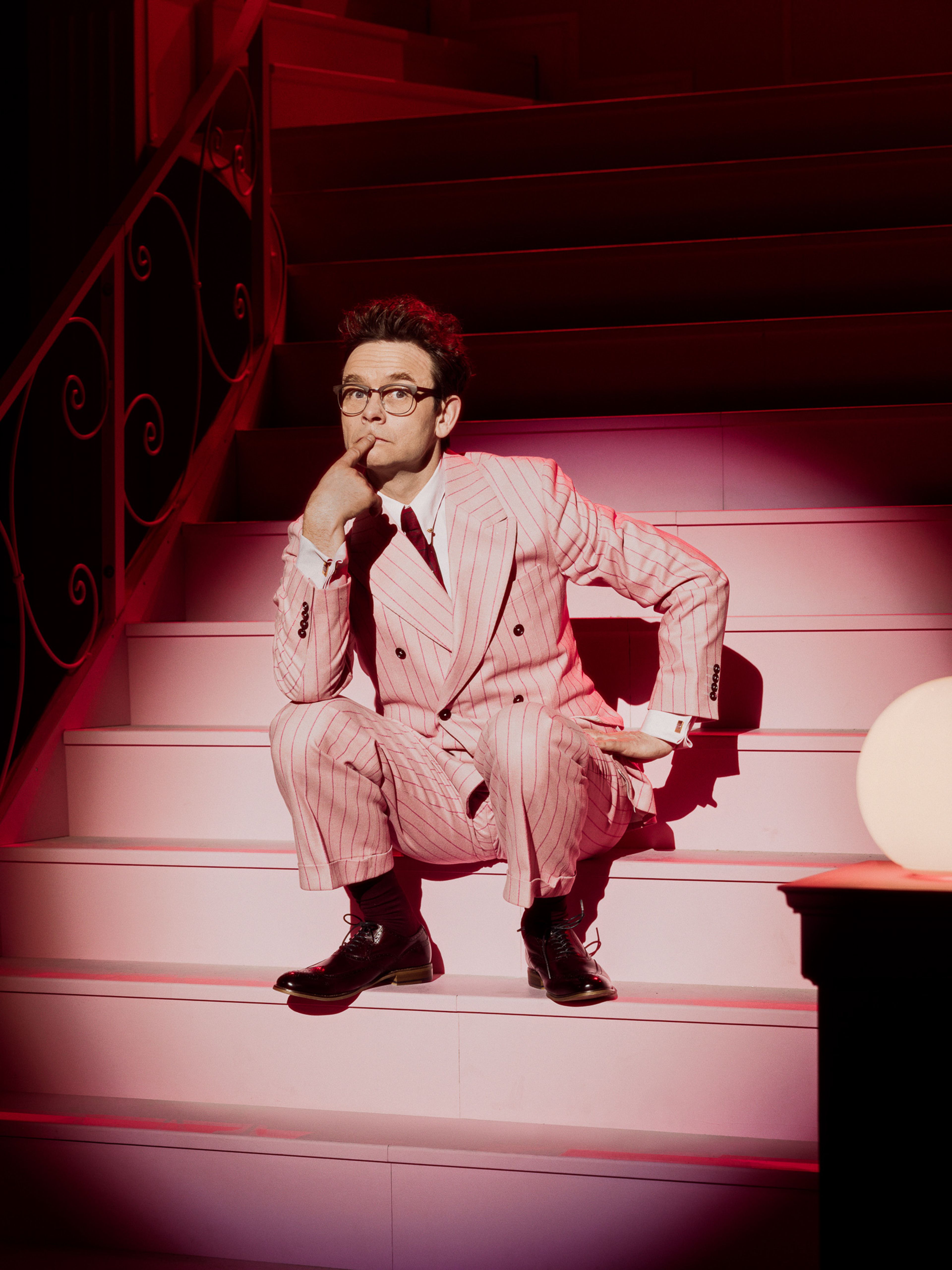Foto av Jan Gunnar Røise i en rosa dress. Han sitter i en trapp på nationaltheateret.