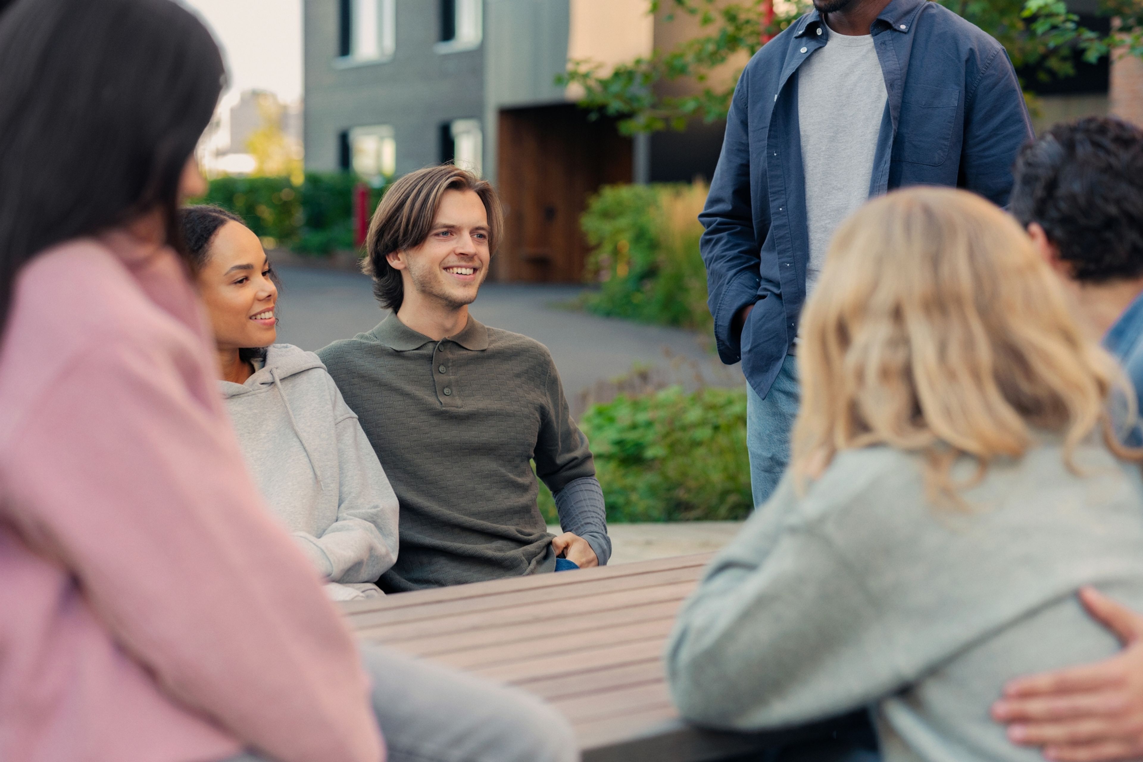 En gruppe beboere sitter ute og snakker sammen i hyggelig lag utenfor boligene sine.