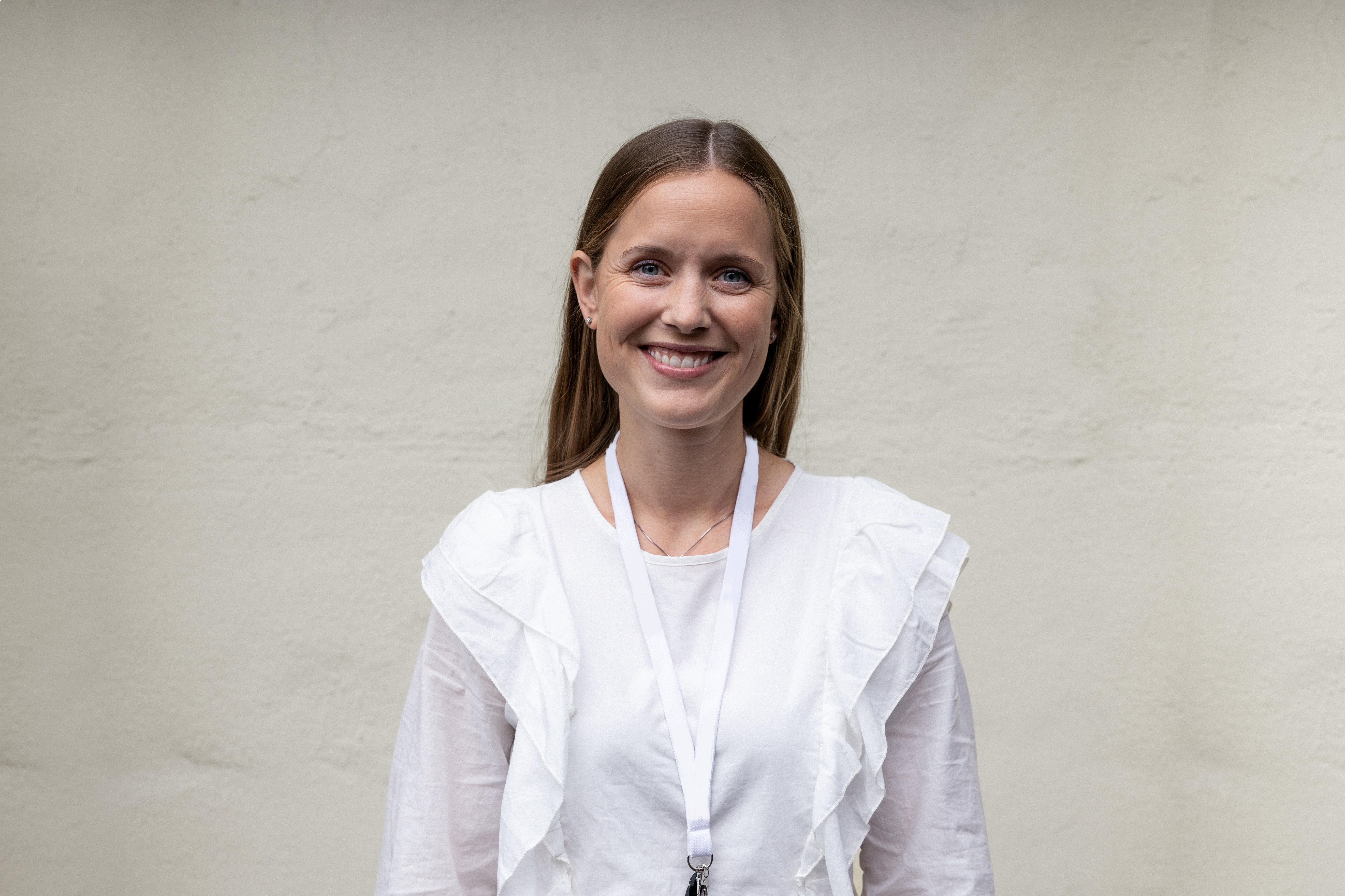 Portrettbilde av en kvinne med brunt hår og hvit bluse som smiler mot kamera