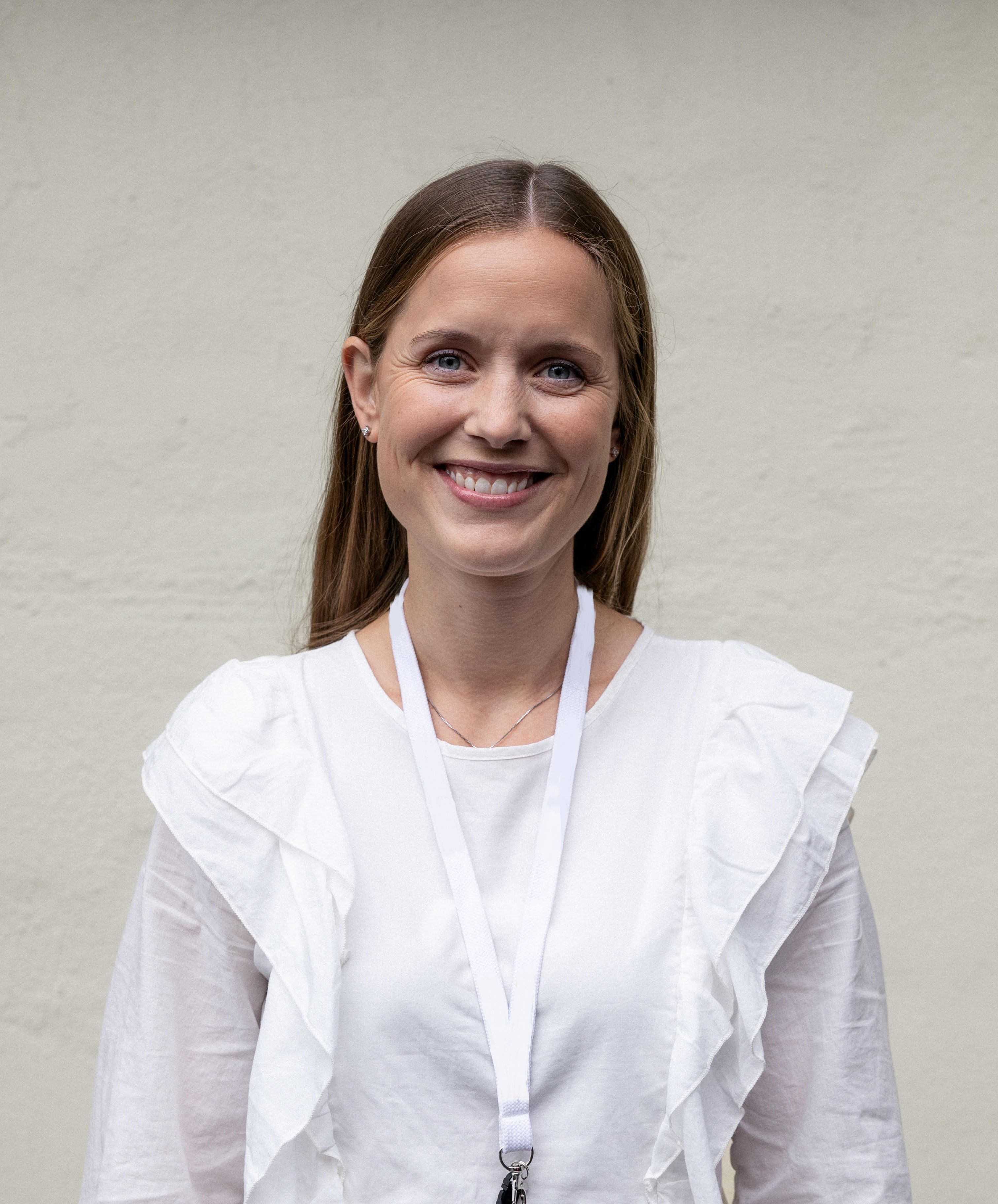 Portrettbilde av en kvinne med brunt hår og hvit bluse som smiler mot kamera