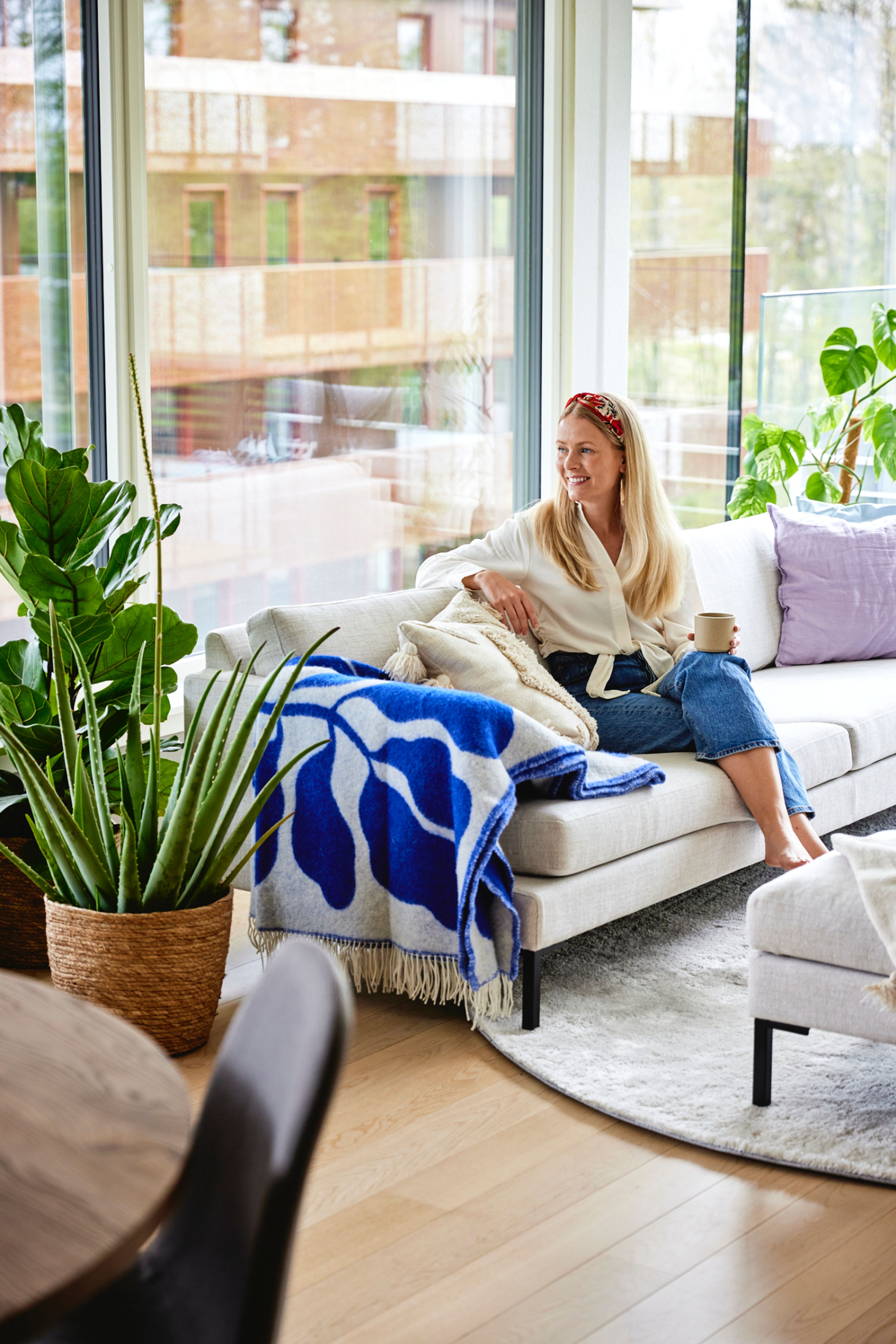 Portrett av Ane sittende i sofaen i stua, med planter i forgrunnen og store vindusflater bak.