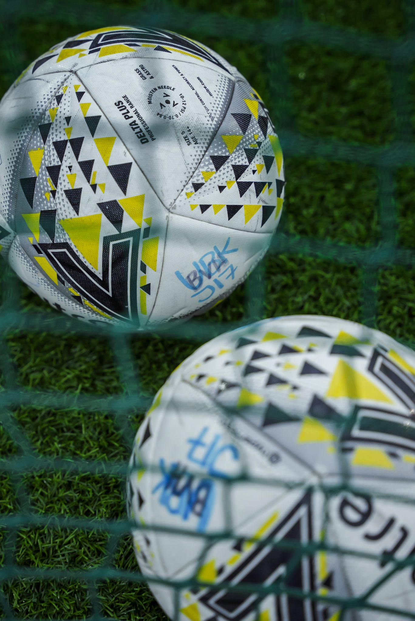 Nærbilde av to mitreballer ovenfra og ned, tatt gjennom nettet på et mål.