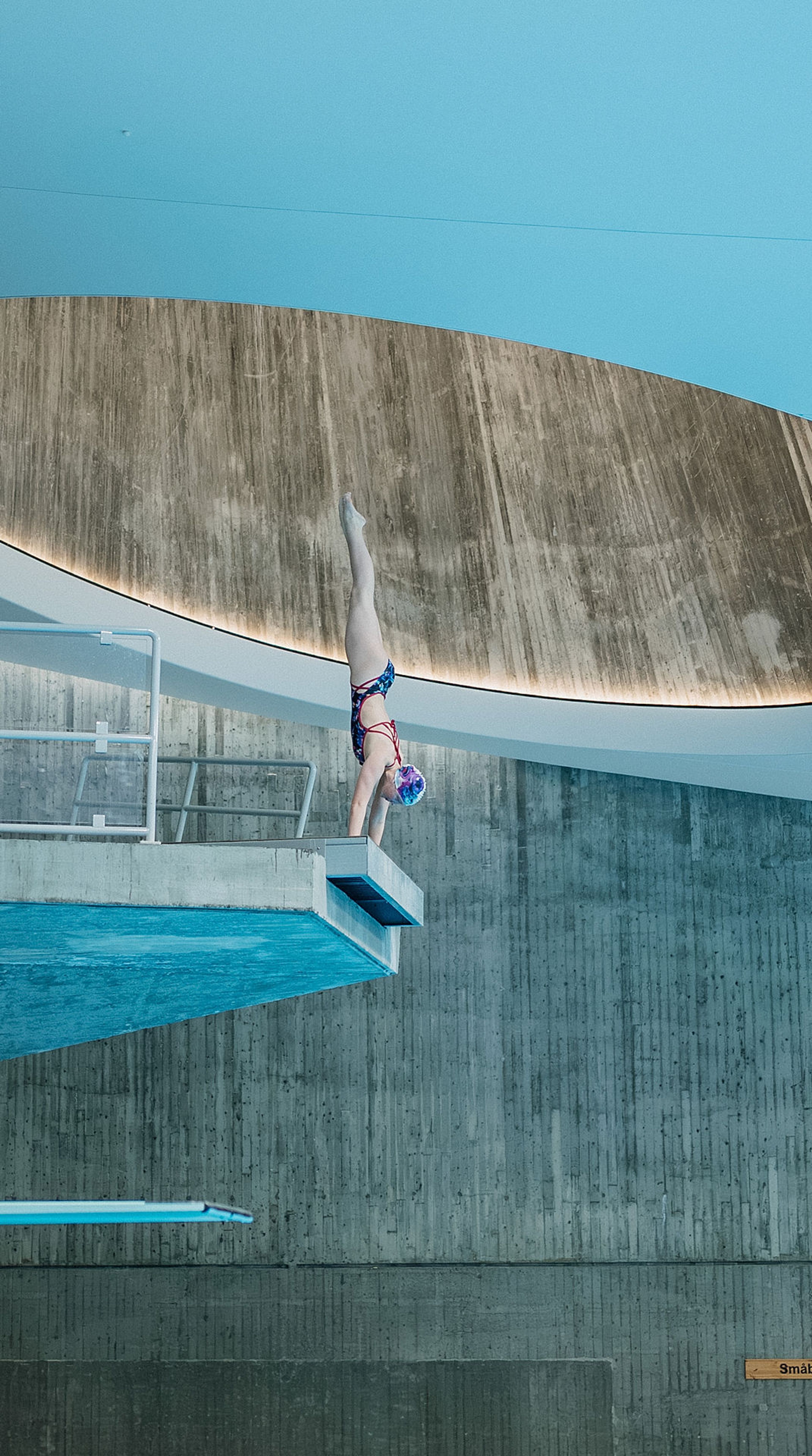 En jente står på henda på stupebrettet og er klar for å slippe seg ned i vannet.