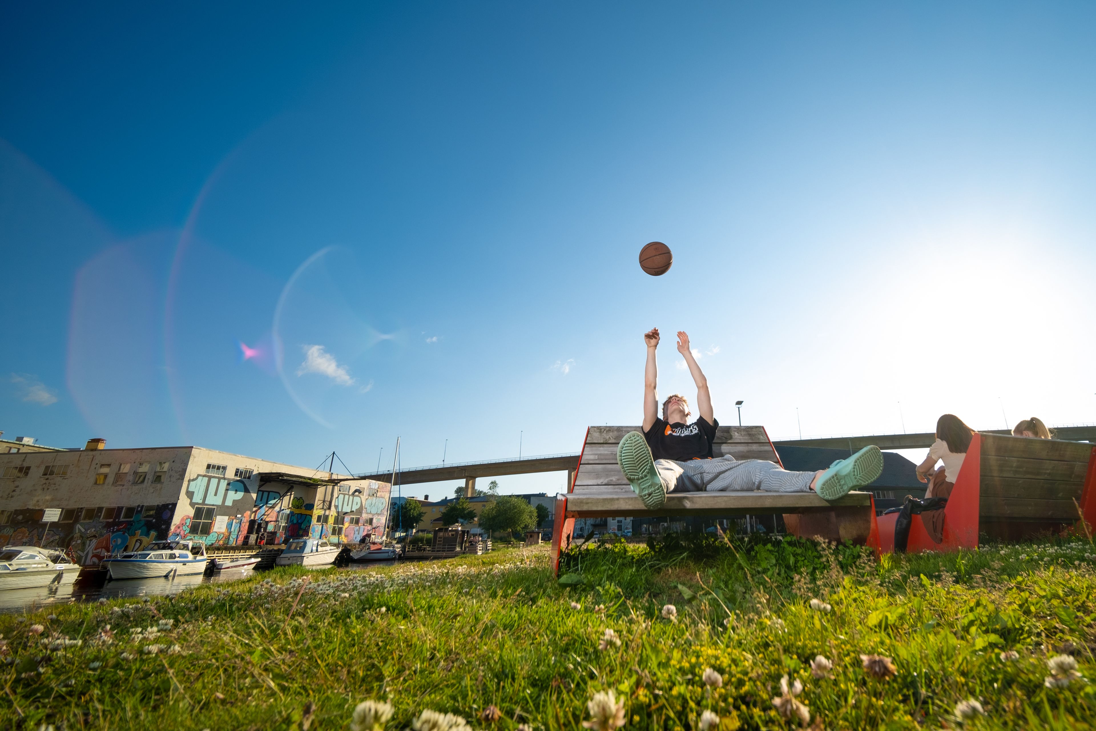 Gutt som kaster basketball mens han sitter i parken i Stavanger