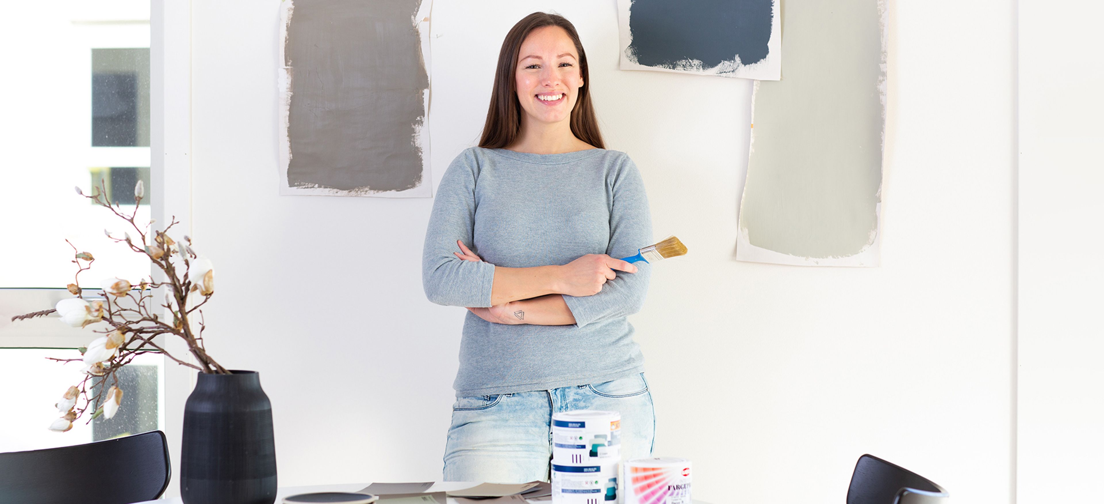 En ung kvinna framför en vägg med målarprover