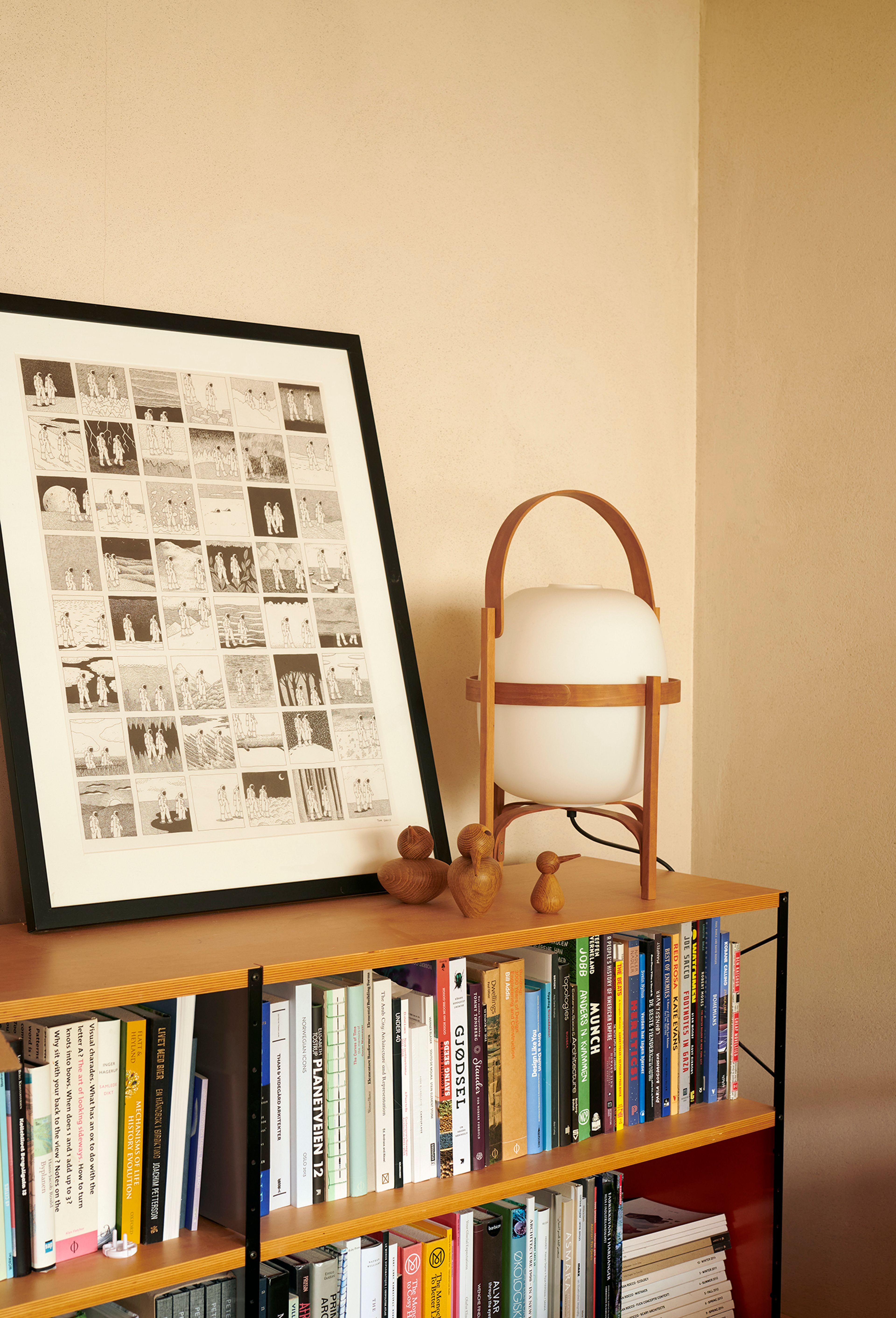 Bokhylle med tegning i ramme og lampe stående oppå.
