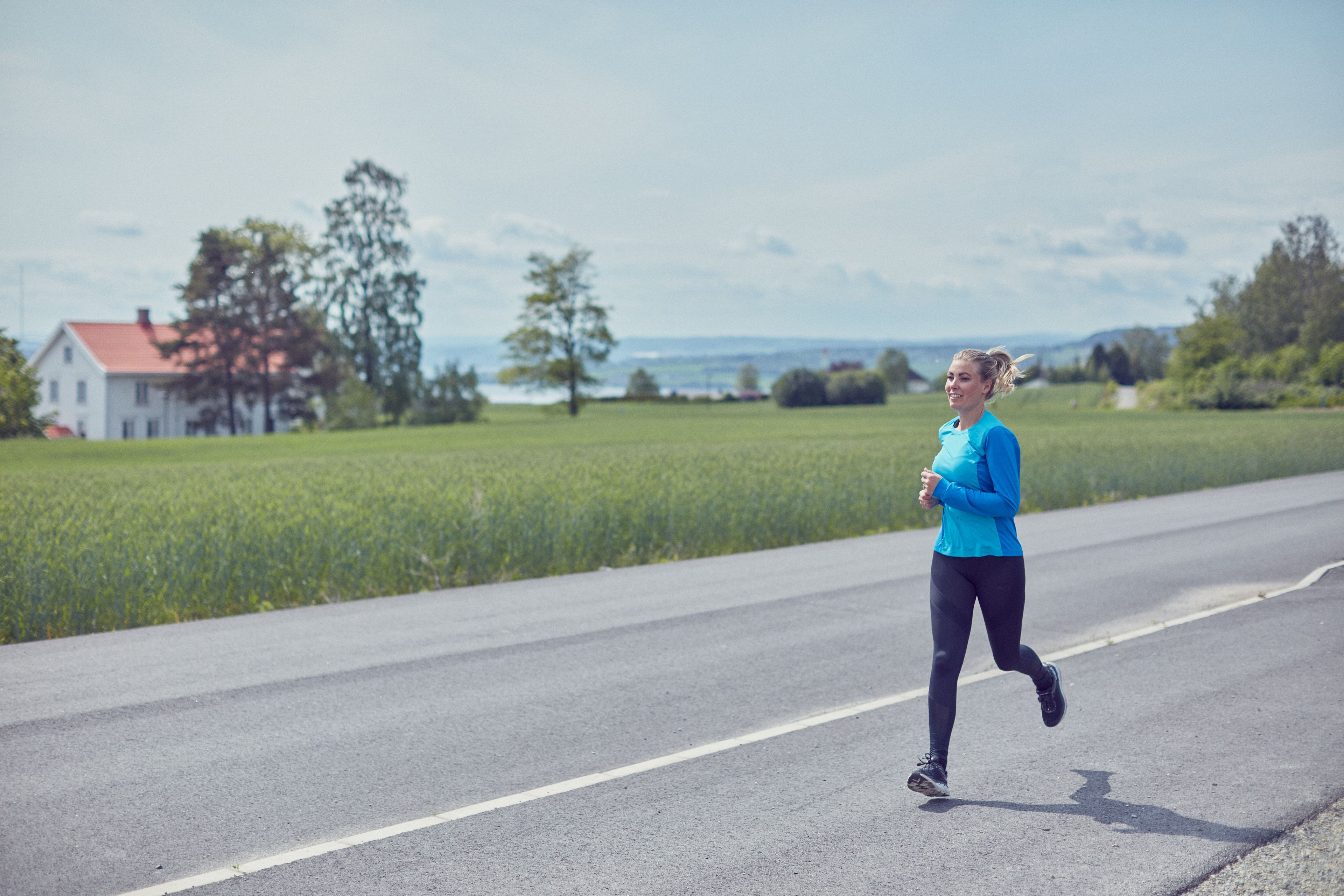 Dame som jogger langs veien med åker i bakgrunn