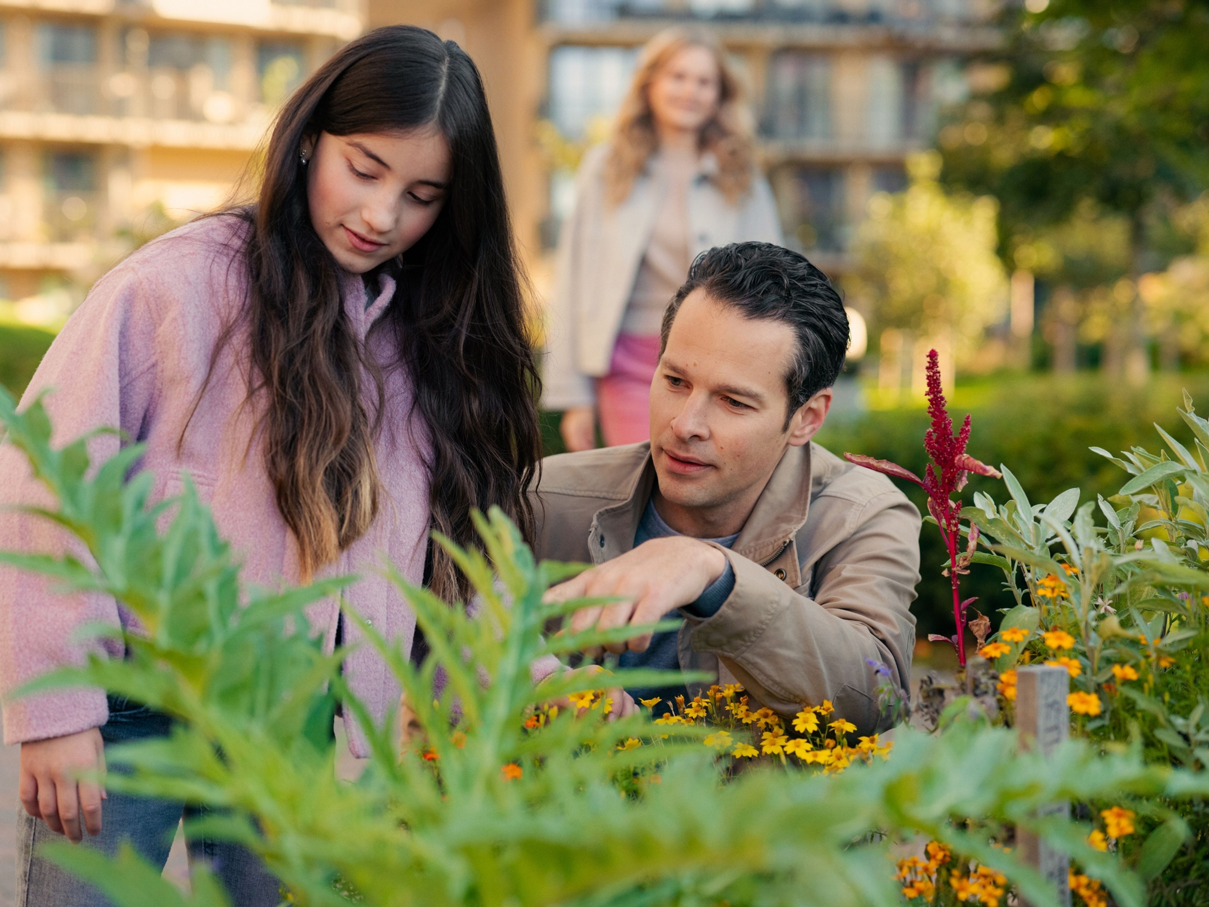 Far og datter er ute i bakgården og ser på grønne planter og gule blomster