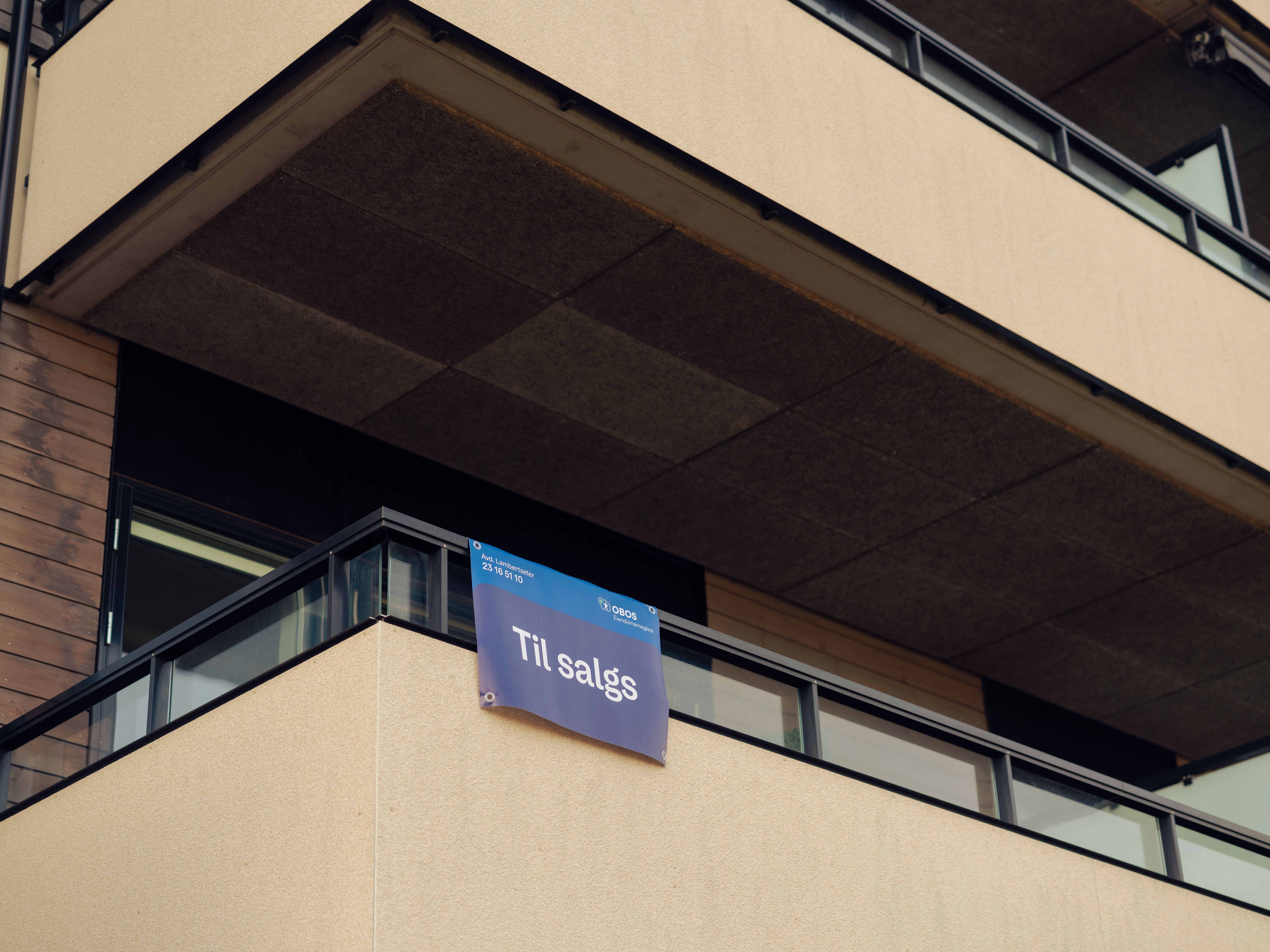 En balkong med et Til salgs-sklt fra OBOS Eiendomsmeglere