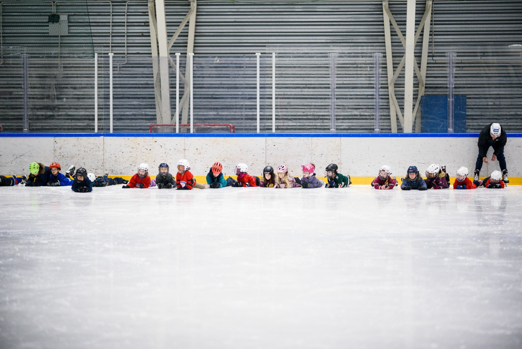 Foto av en lang rekke med barn som har lagt seg ned på magen på skøyteisen.