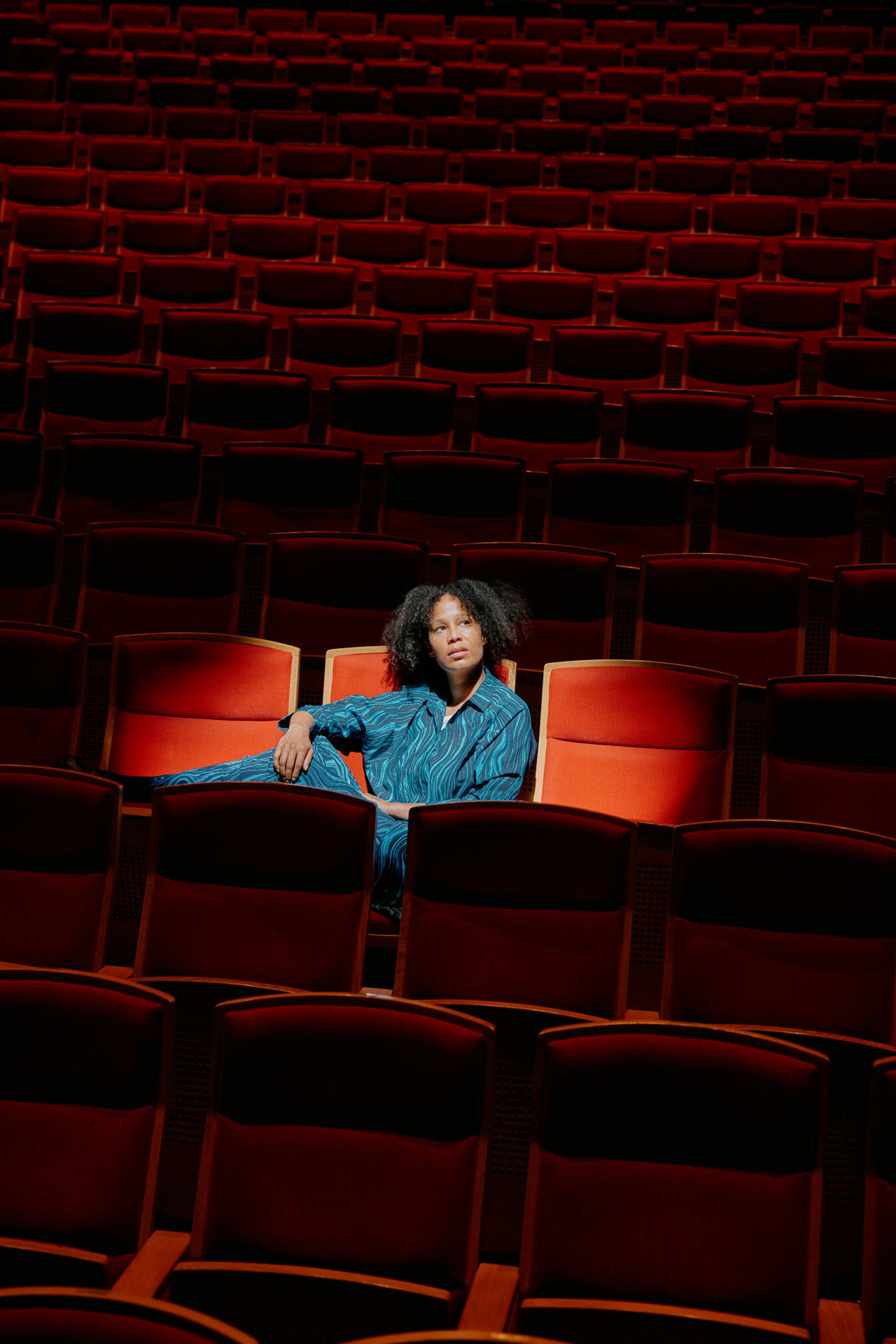 Mimmi Tamba sitter i en stol i salen der hun spiller teater