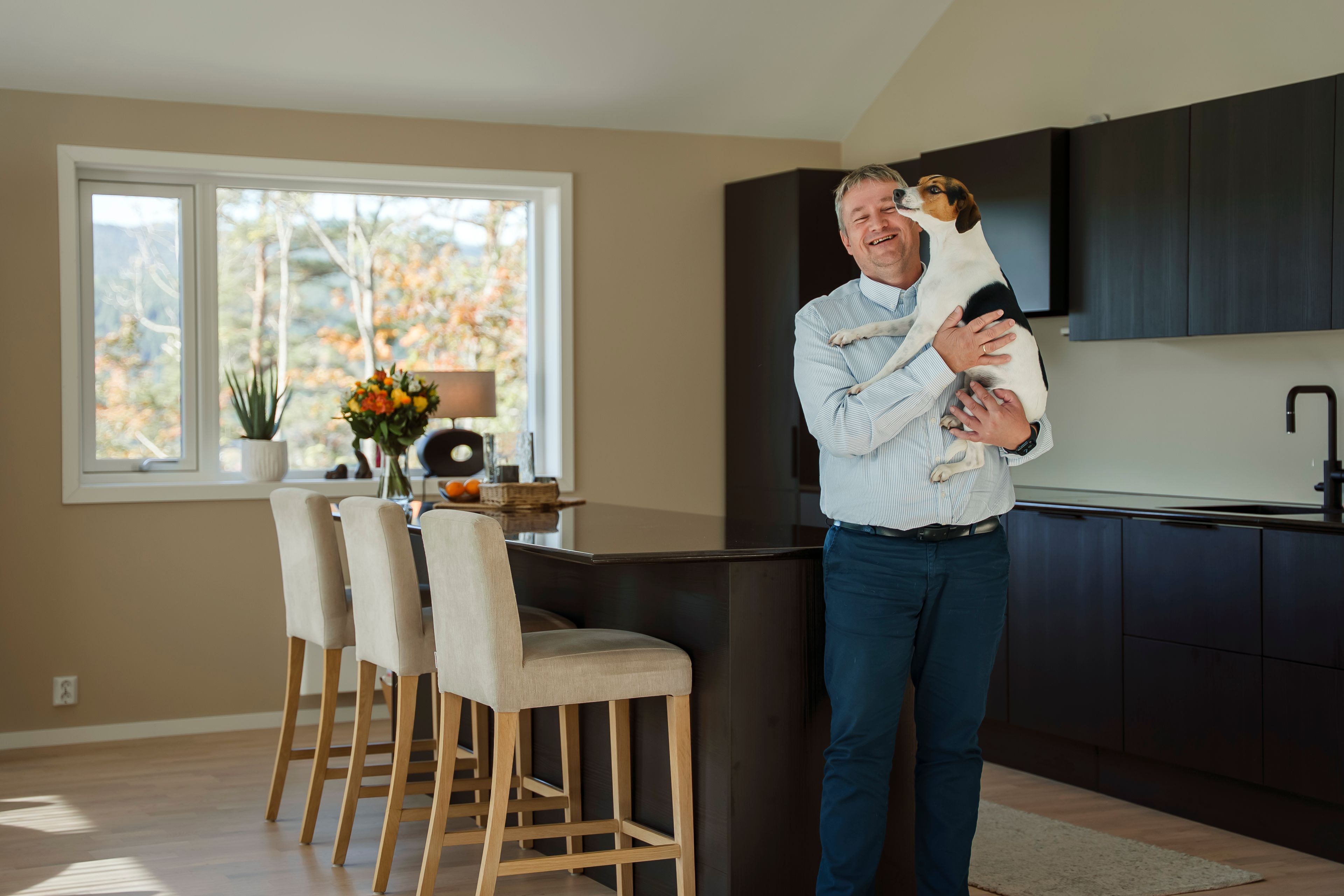Mann står lent inntil kjøkkenøya og smiler mens han holder den lille hunden sin