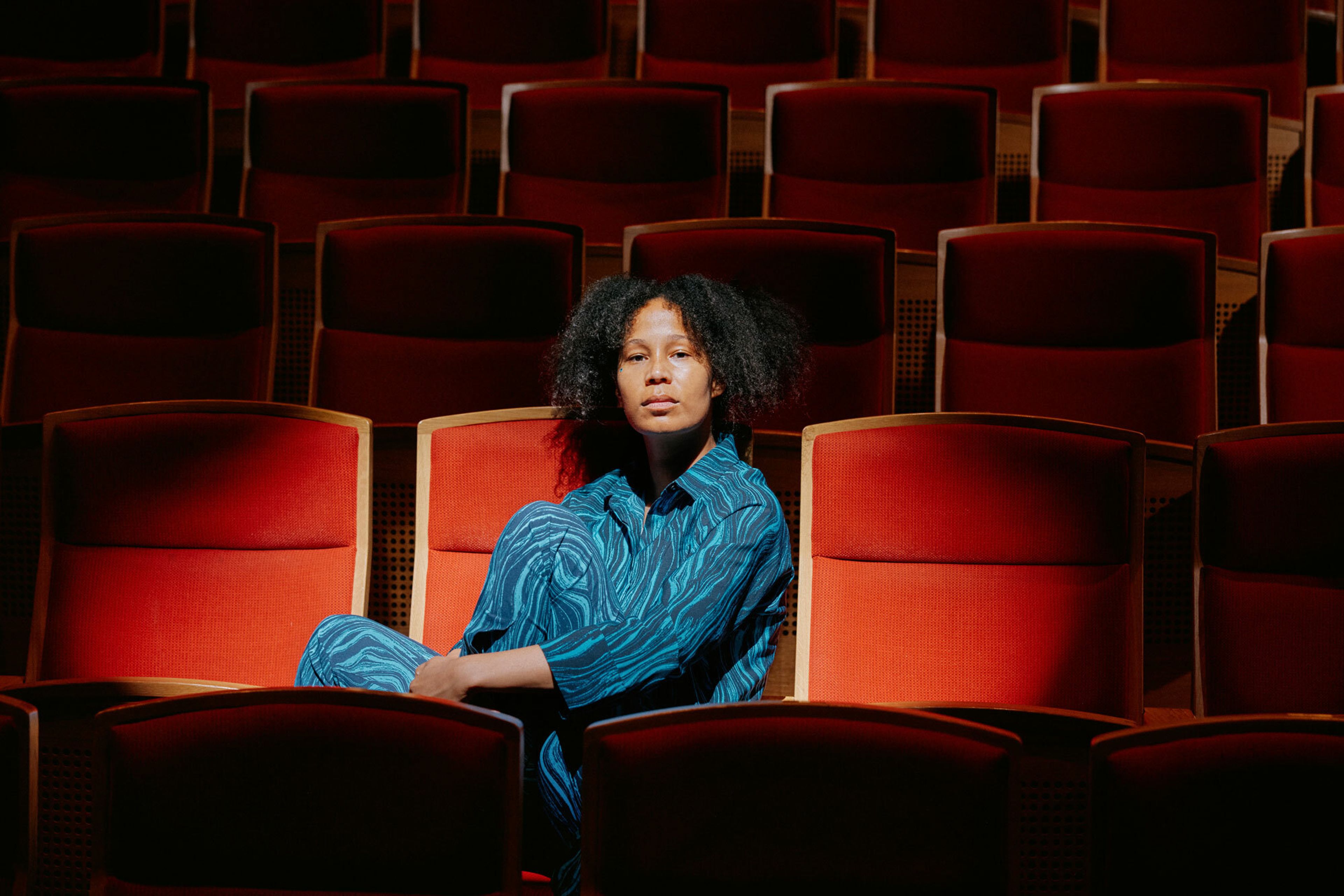 Mimmi Tamba sitter i en rød stol i salen der hun spiller teater