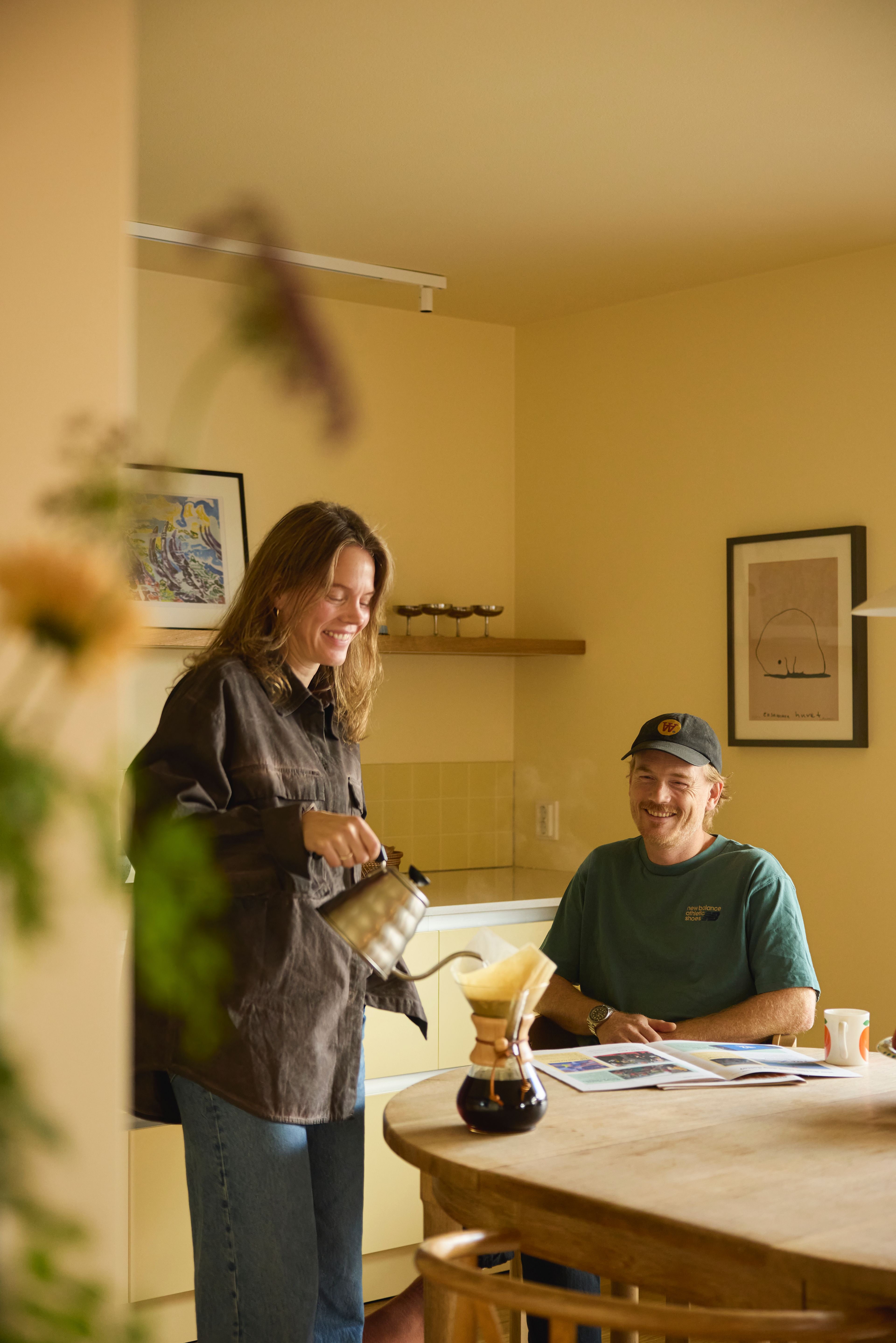 Anette og Jonas smilende på kjøkkenet. Anette sjenker kaffe. 