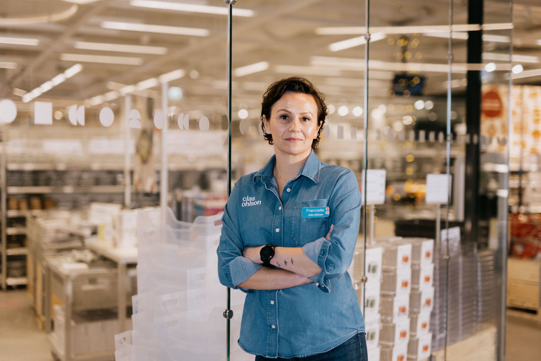Breddebilde av butikksjef Francielle Lubke som lener seg mot butikken sin glassvegg mens hun har armene i kors