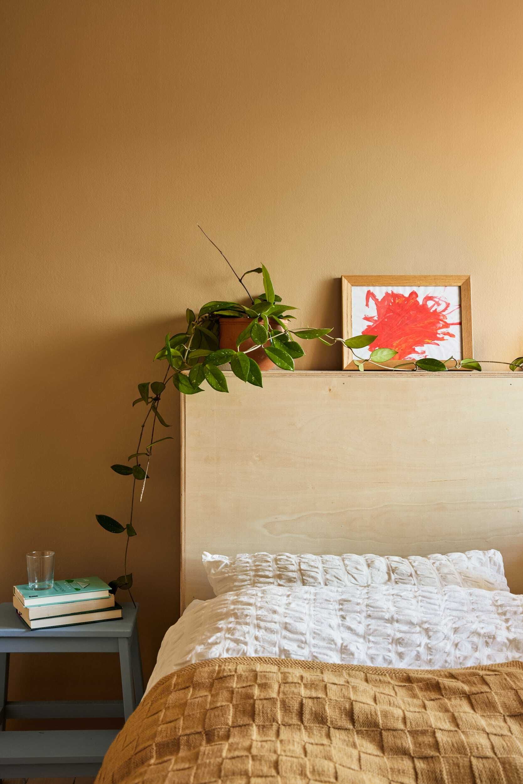 Seng og sengegavl med ulike dekorasjoner oppå, gule vegger.